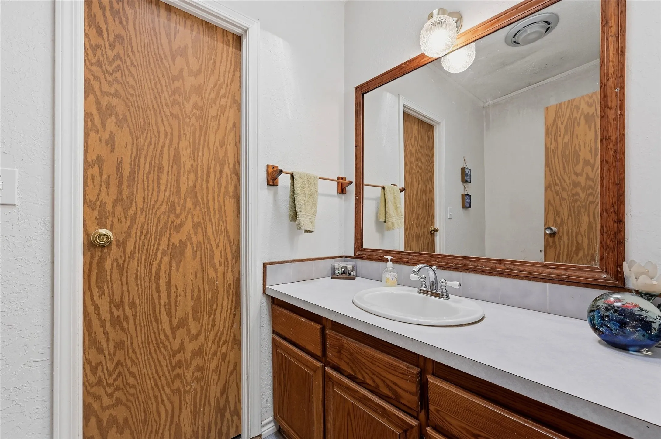 Bathroom vanity featuring a white countertop with an integrated oval sink, wood-finish cabinetry, and a framed mirror