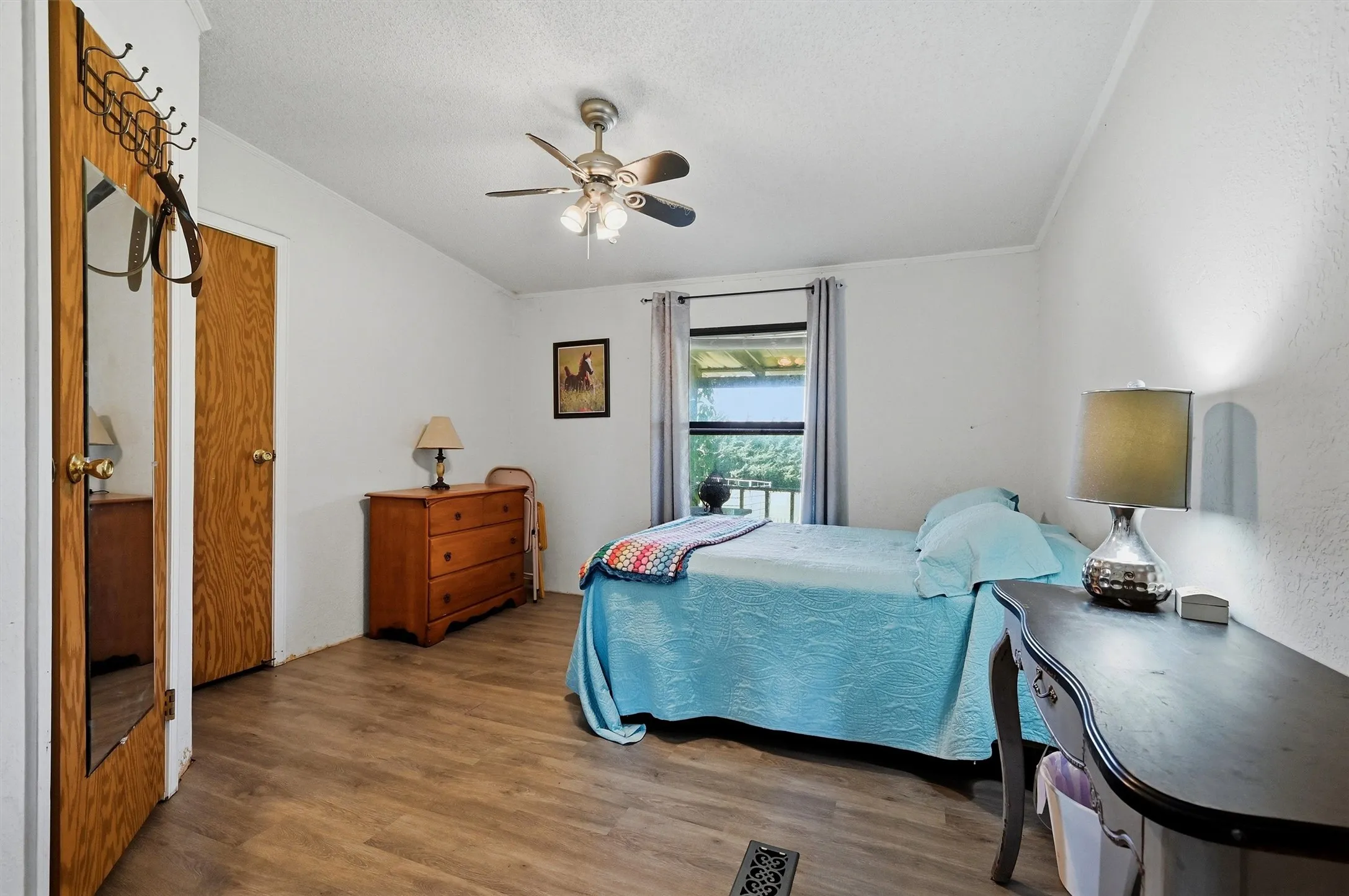 Bedroom featuring wood-finish flooring, a ceiling fan with light fixture, and a window with gray curtains