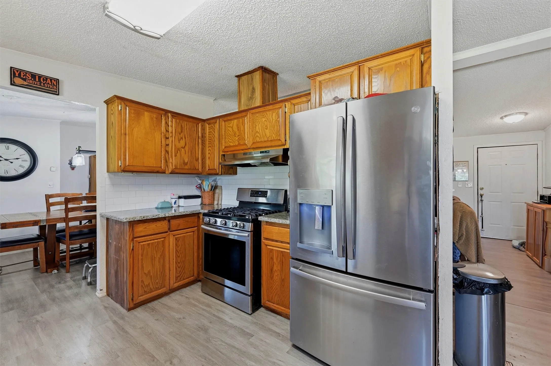 Kitchen featuring wood-finish cabinetry, stainless steel appliances, granite countertops, white subway tile backsplash, and wood-finish flooring