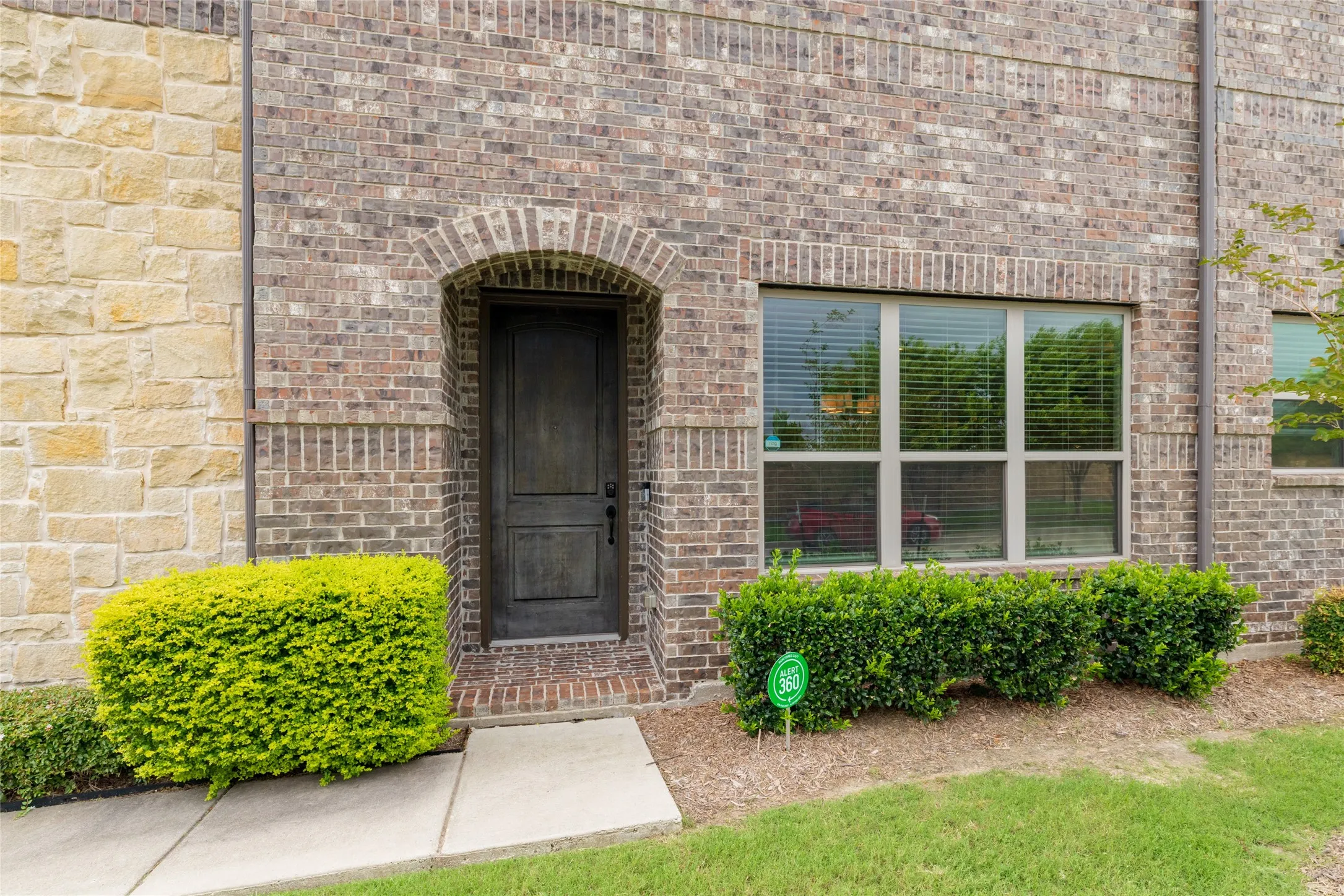 Brick and stone facade featuring an arched entryway, dark panel door, and large window with blinds