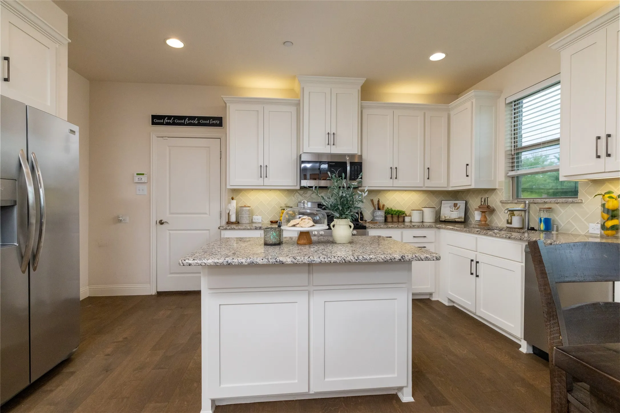 Well-appointed kitchen featuring a central island with countertop, ample white cabinetry, stainless steel appliances, herringbone tile backsplash, and wood-finish flooring