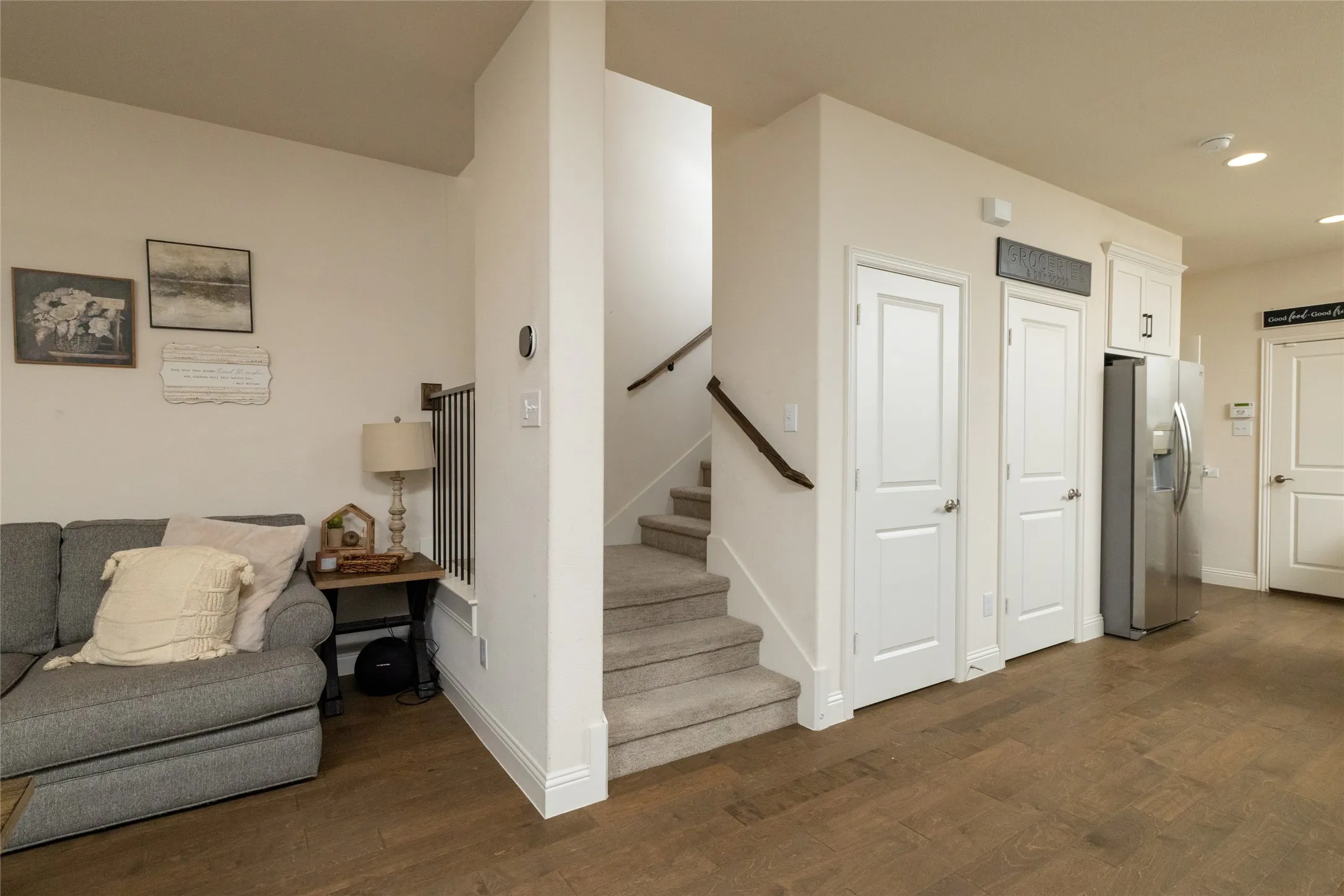 Open-concept interior featuring wood-finish flooring, white trim, a carpeted staircase with dark metal balusters and a wood handrail, and white paneled doors