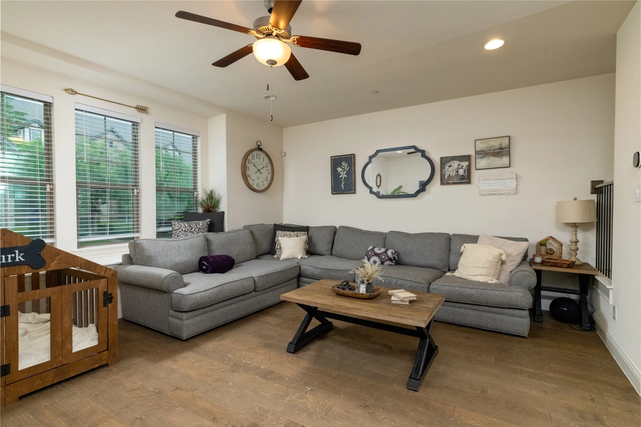 Spacious living area featuring wood-finish flooring, ample natural light from multiple windows, and a ceiling fan.