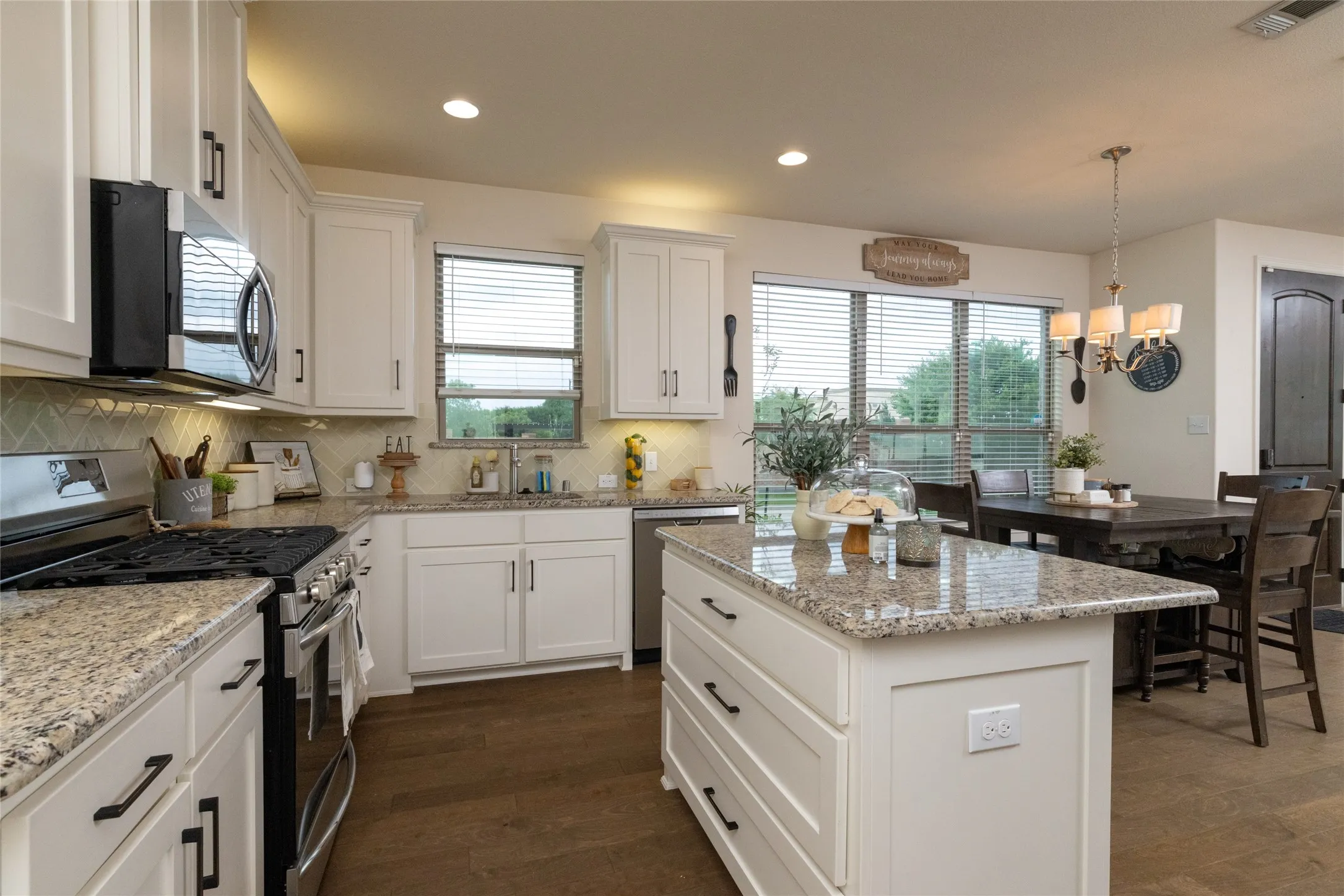 Expansive kitchen with a large central island, granite countertops, white cabinetry, and stainless steel appliances