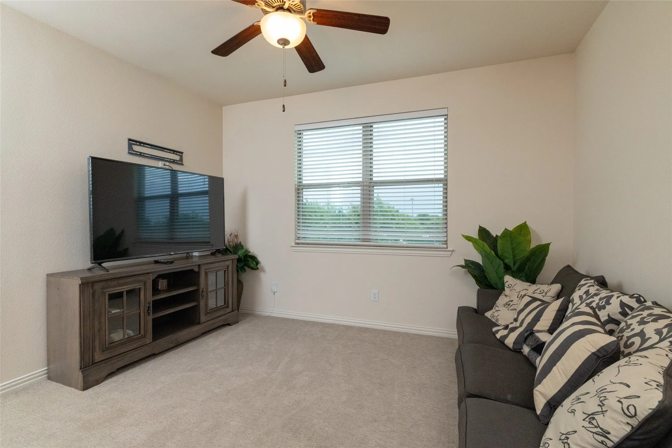 Carpeted room featuring a ceiling fan with integrated lighting, a window with horizontal blinds, and neutral-toned walls