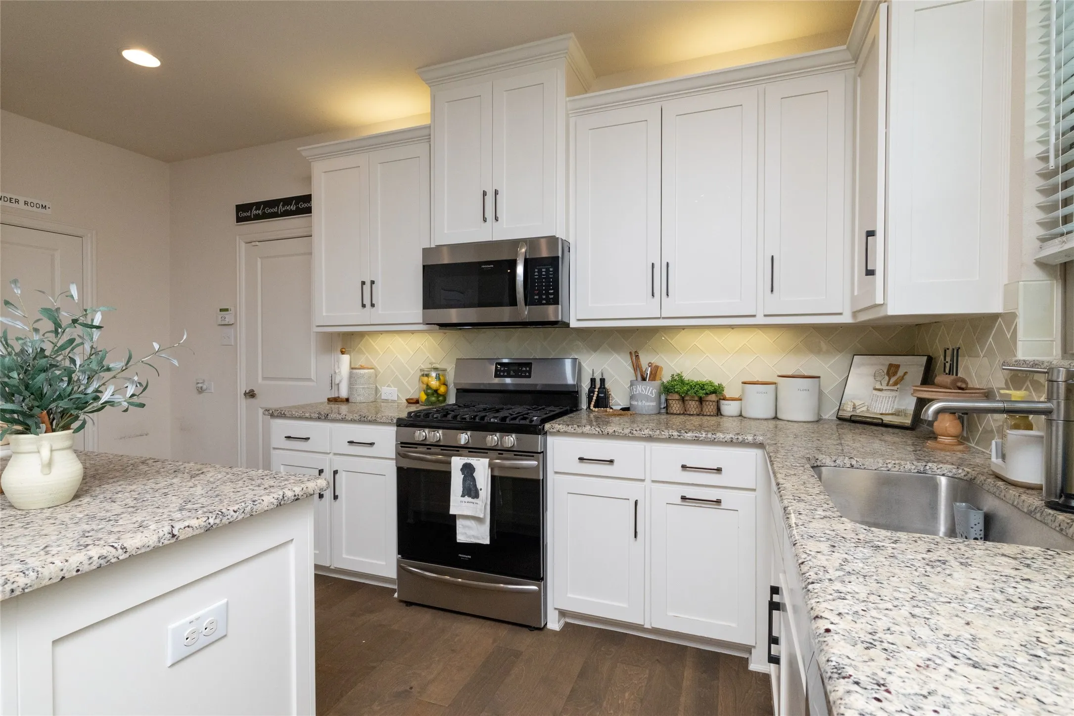 Well-appointed kitchen featuring white cabinetry, stainless steel appliances, granite countertops, a tiled backsplash, and wood-finish flooring