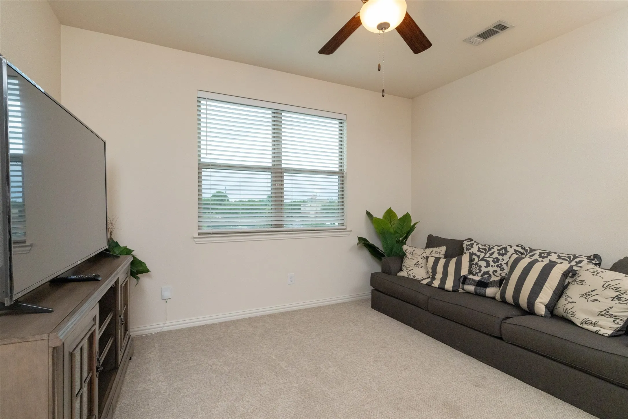 Carpeted room featuring a ceiling fan with integrated lighting, a window with horizontal blinds, and neutral-toned walls