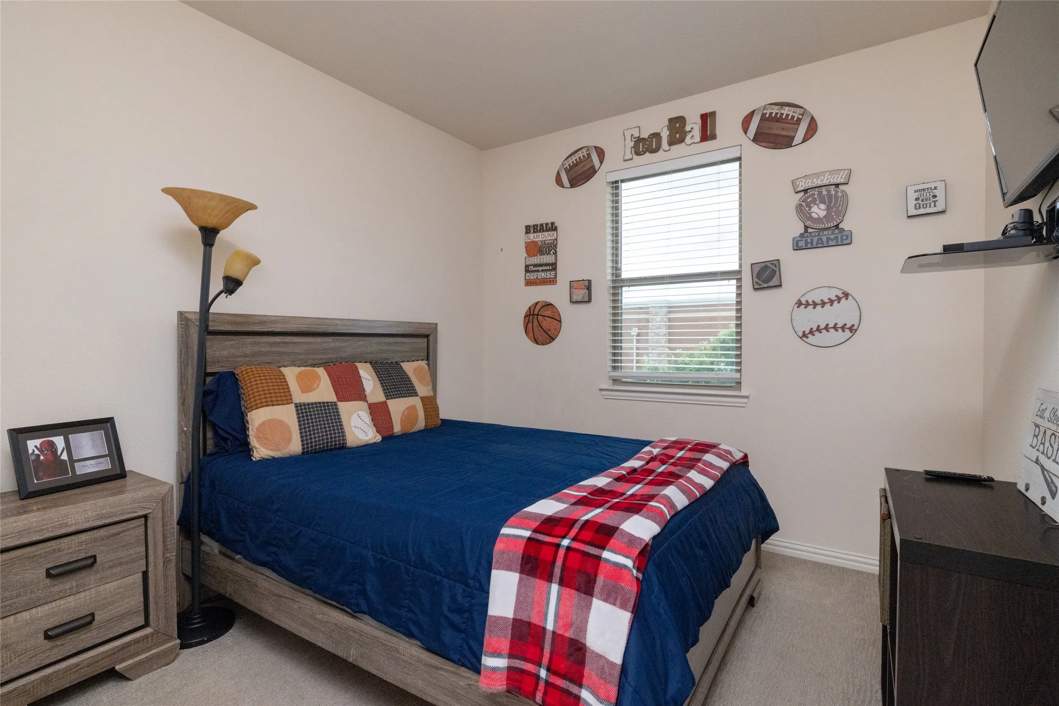 Bright interior room featuring a window with horizontal blinds, light-toned carpeting, and a built-in wall shelf