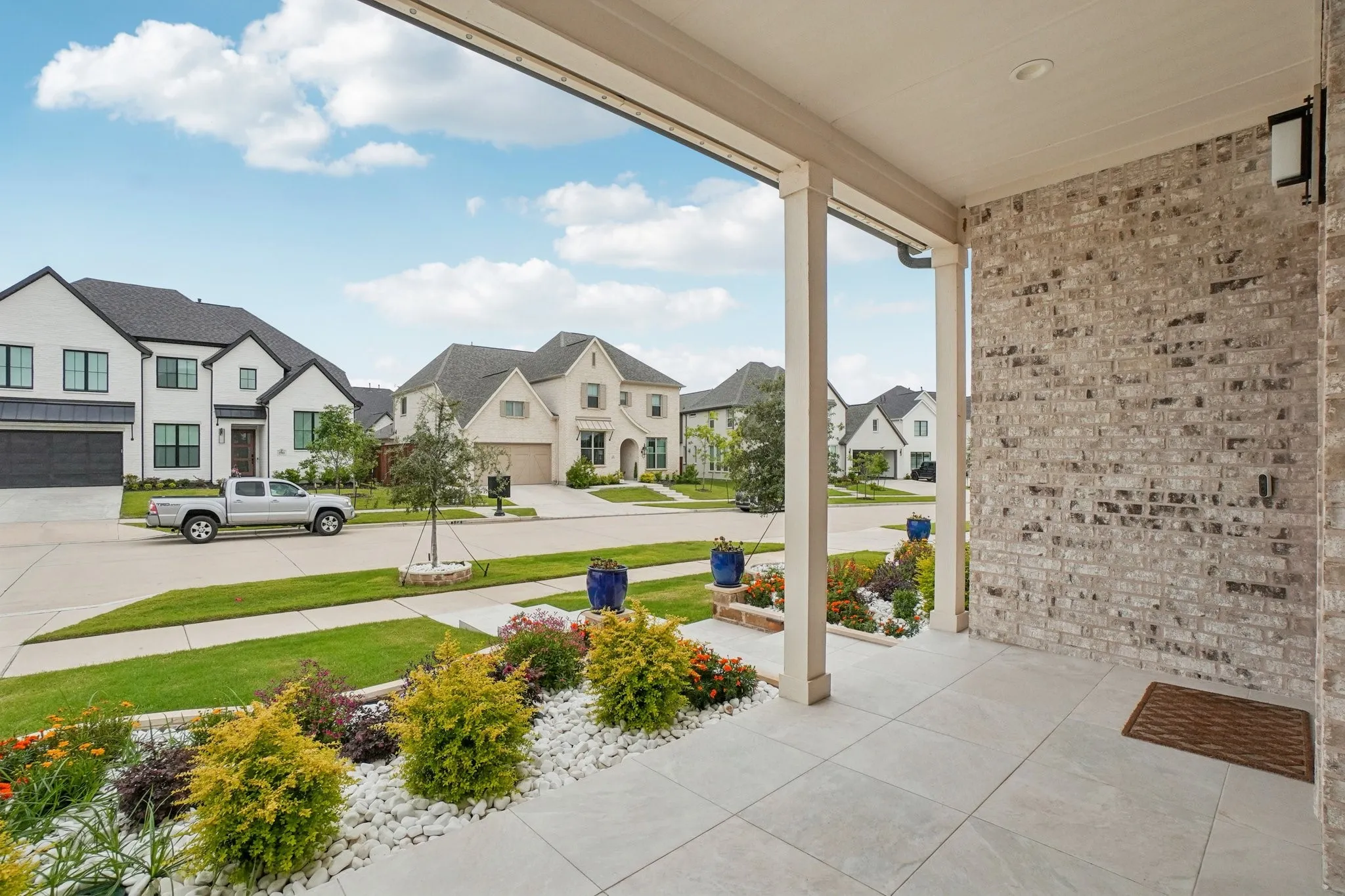 Covered front porch featuring light-colored brick siding, recessed lighting, and large format floor tiles