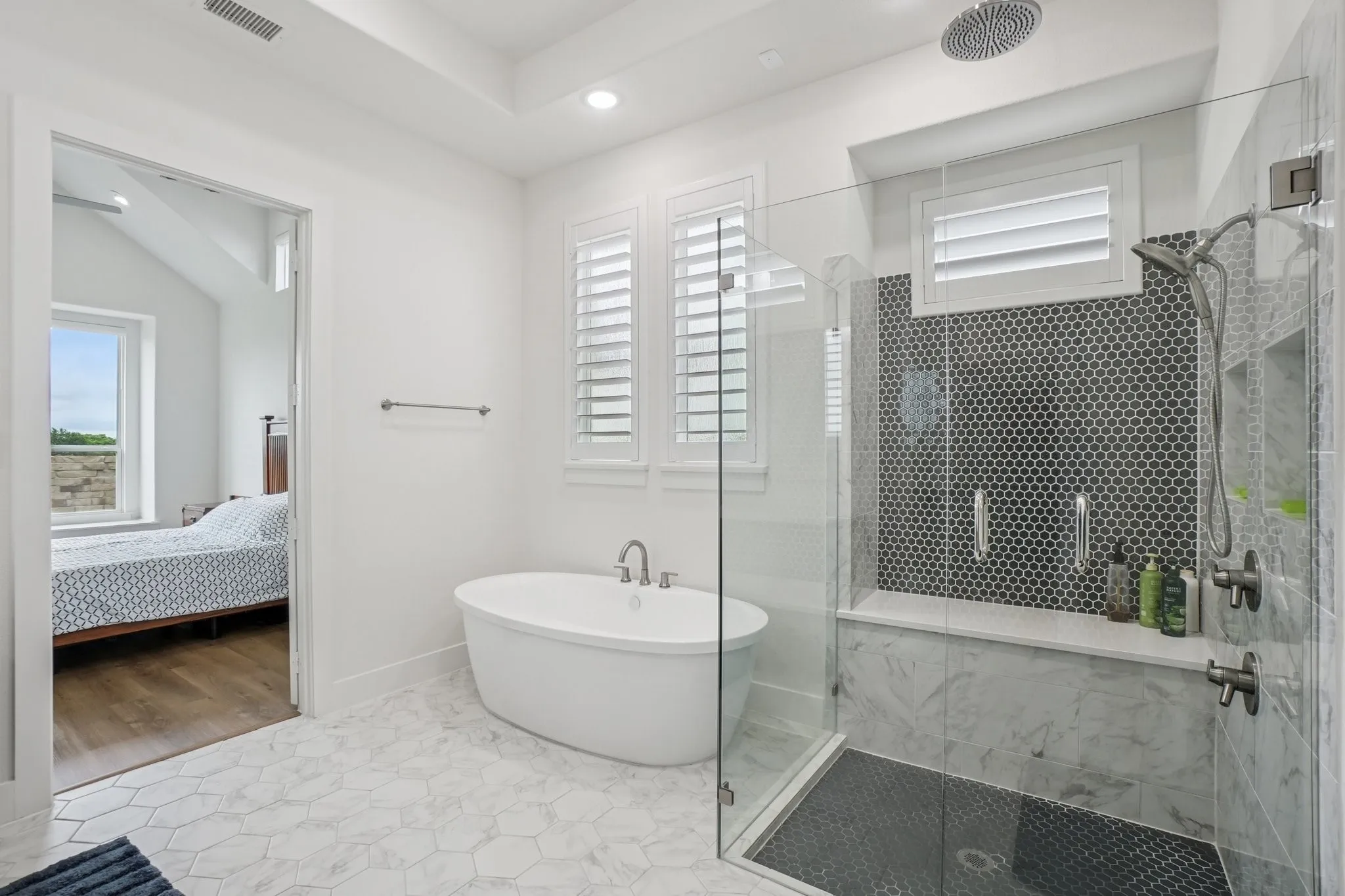 Bathroom featuring a freestanding oval tub, a walk-in shower with clear glass enclosure and dark hexagonal tile, and hexagonal marble-look floor tiles