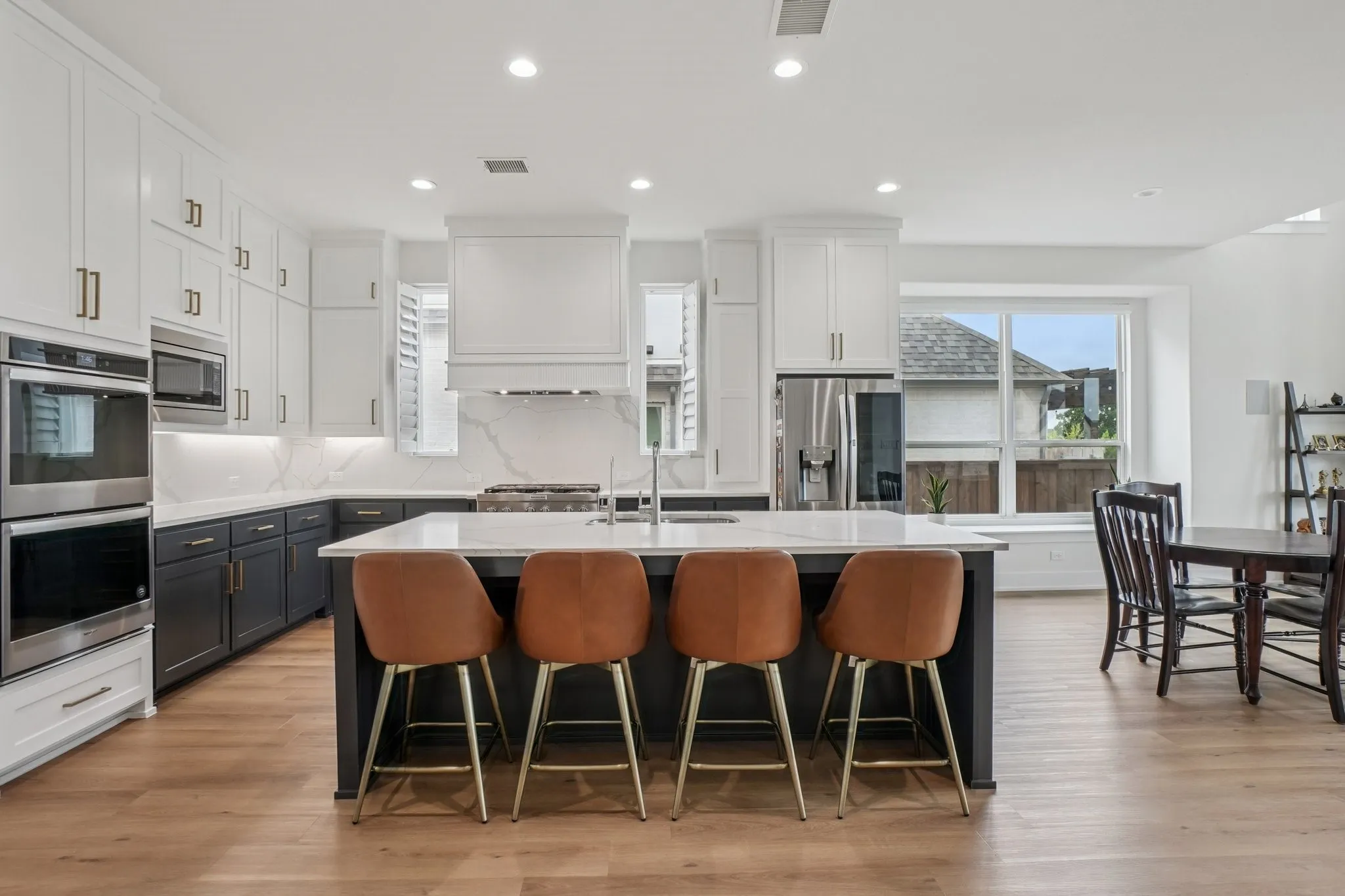 Gourmet kitchen featuring a large central island, double wall ovens, built-in microwave, white shaker cabinetry, and wood-finish flooring
