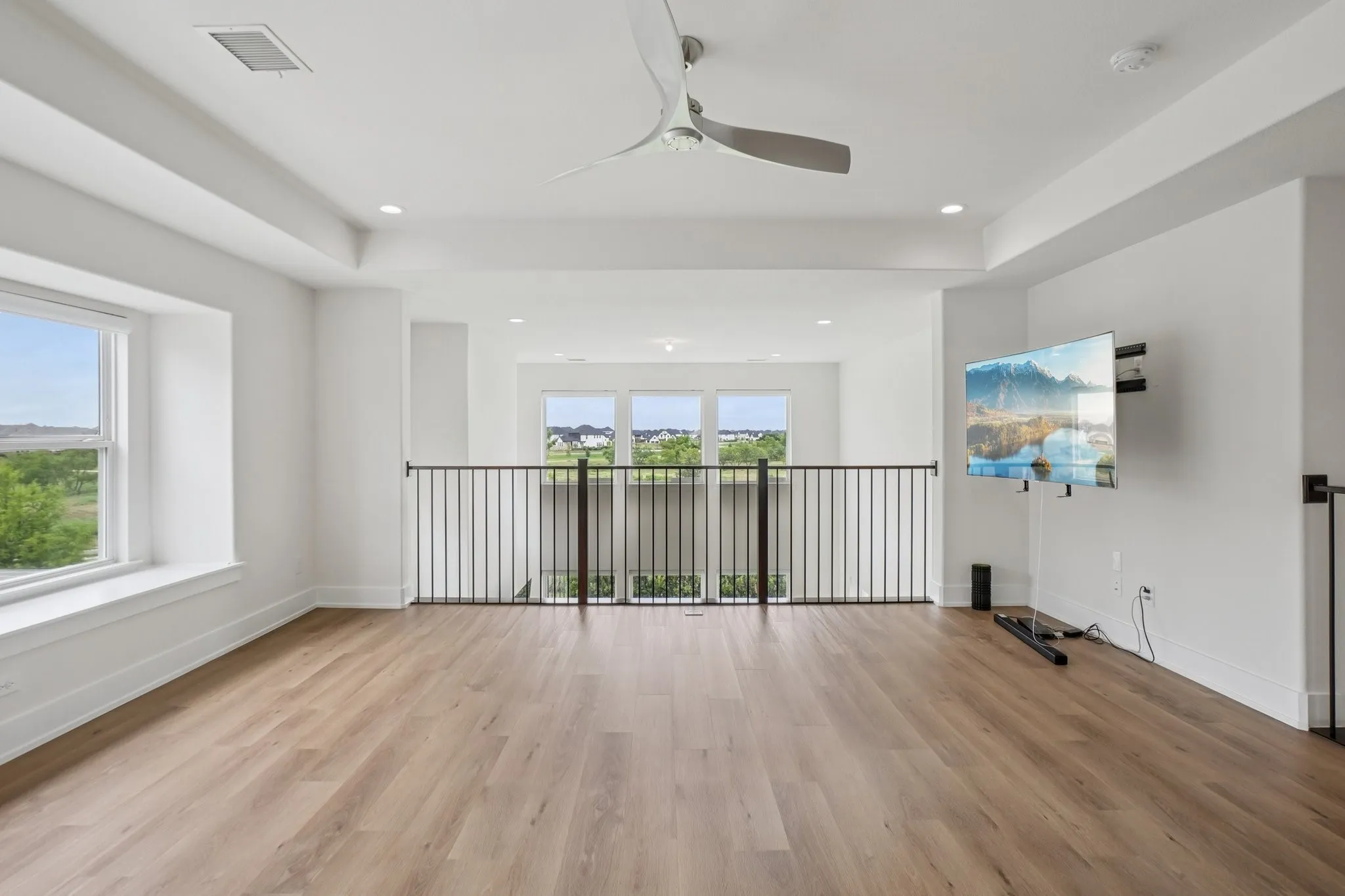 Spacious open loft area featuring wood-finish flooring, recessed lighting, and a contemporary ceiling fan