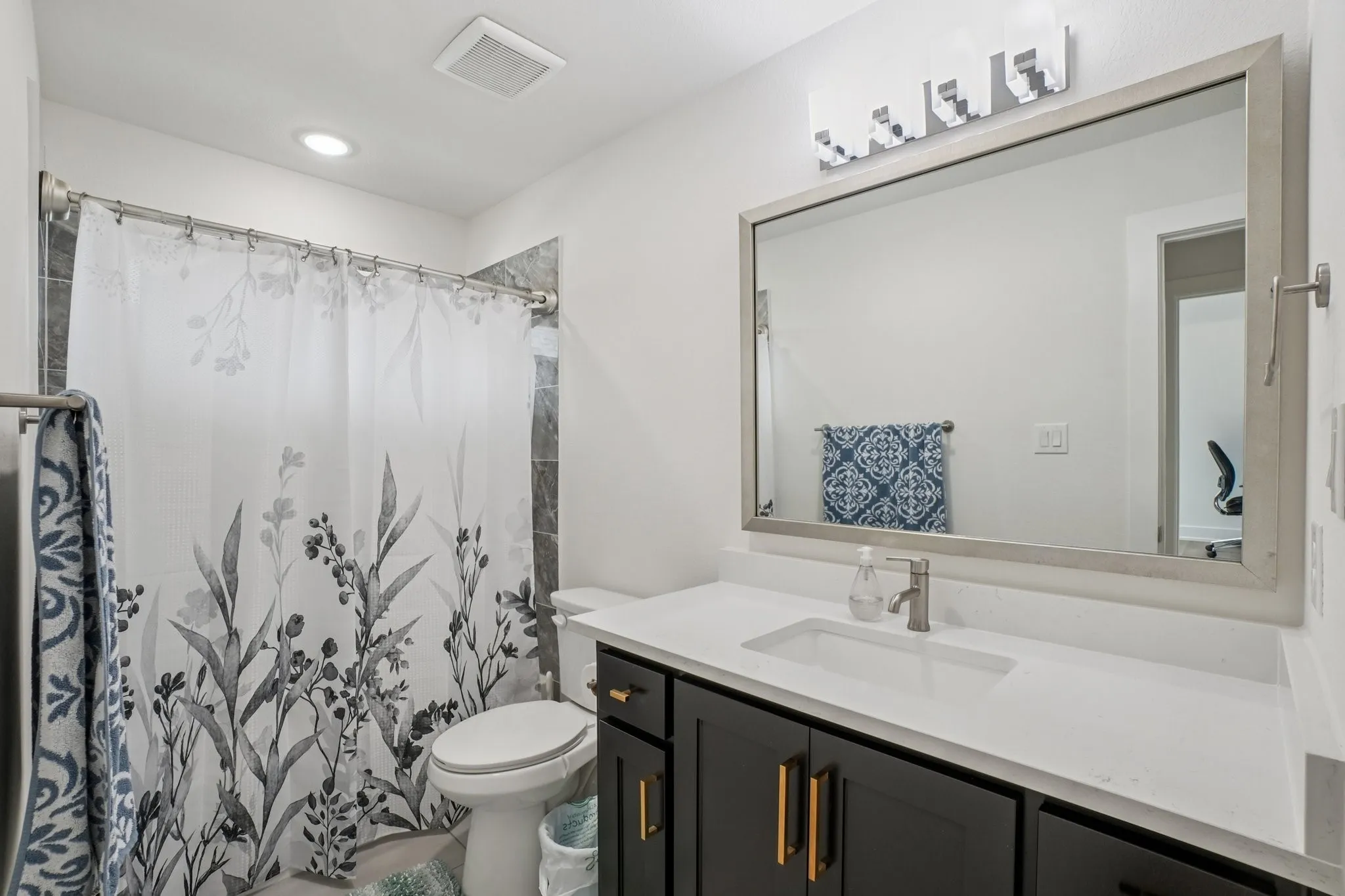 Contemporary bathroom featuring a dark wood-finish vanity with gold-tone hardware, a white undermount sink, and a light-toned countertop