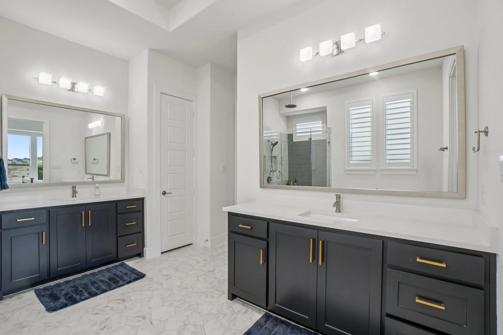 Spacious bathroom featuring dual vanities with dark cabinetry, white countertops, and brushed brass hardware