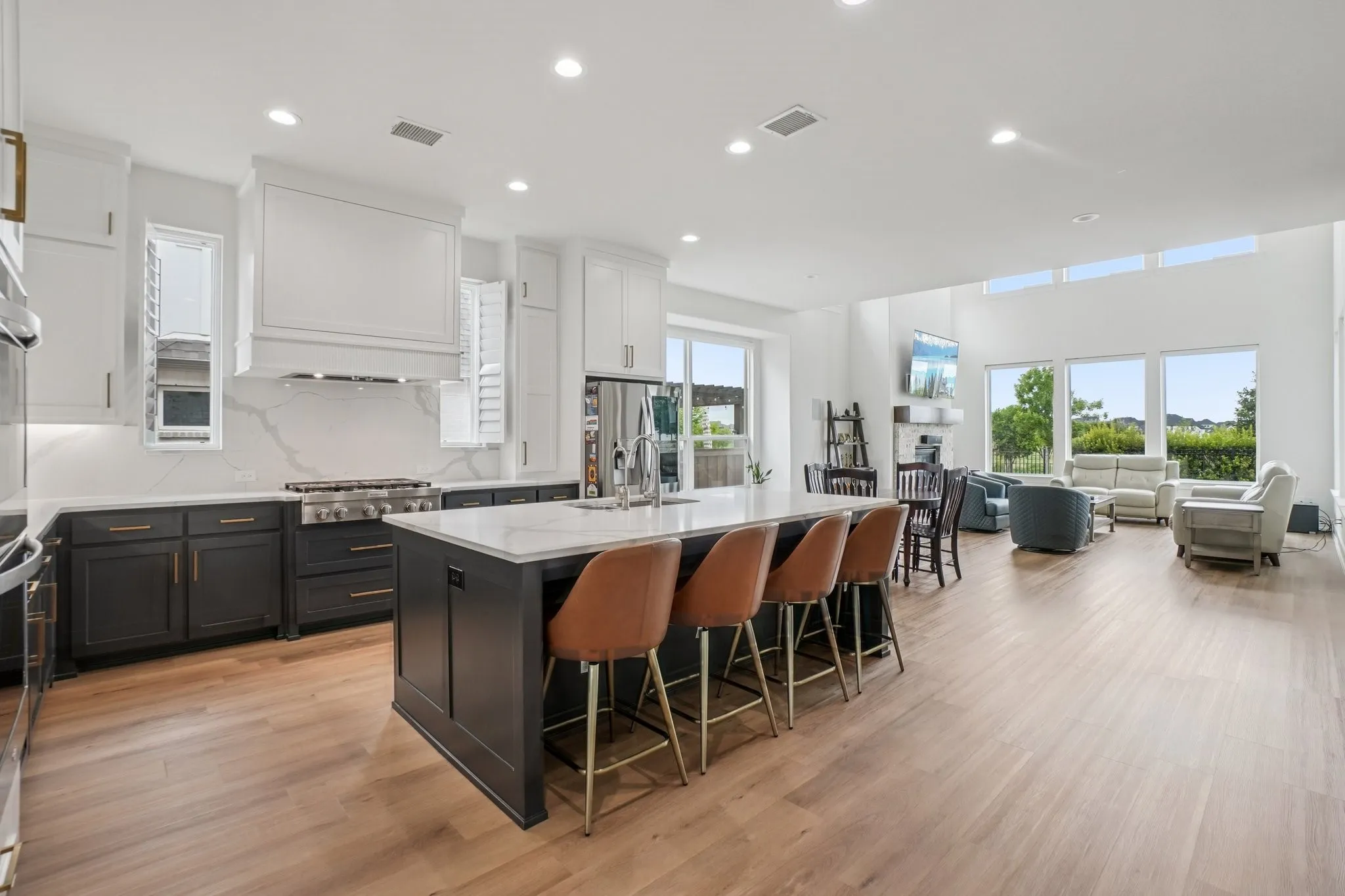 Open-concept kitchen featuring an oversized island with seating, a gas range with a decorative range hood, two-tone cabinetry, and wood-finish flooring