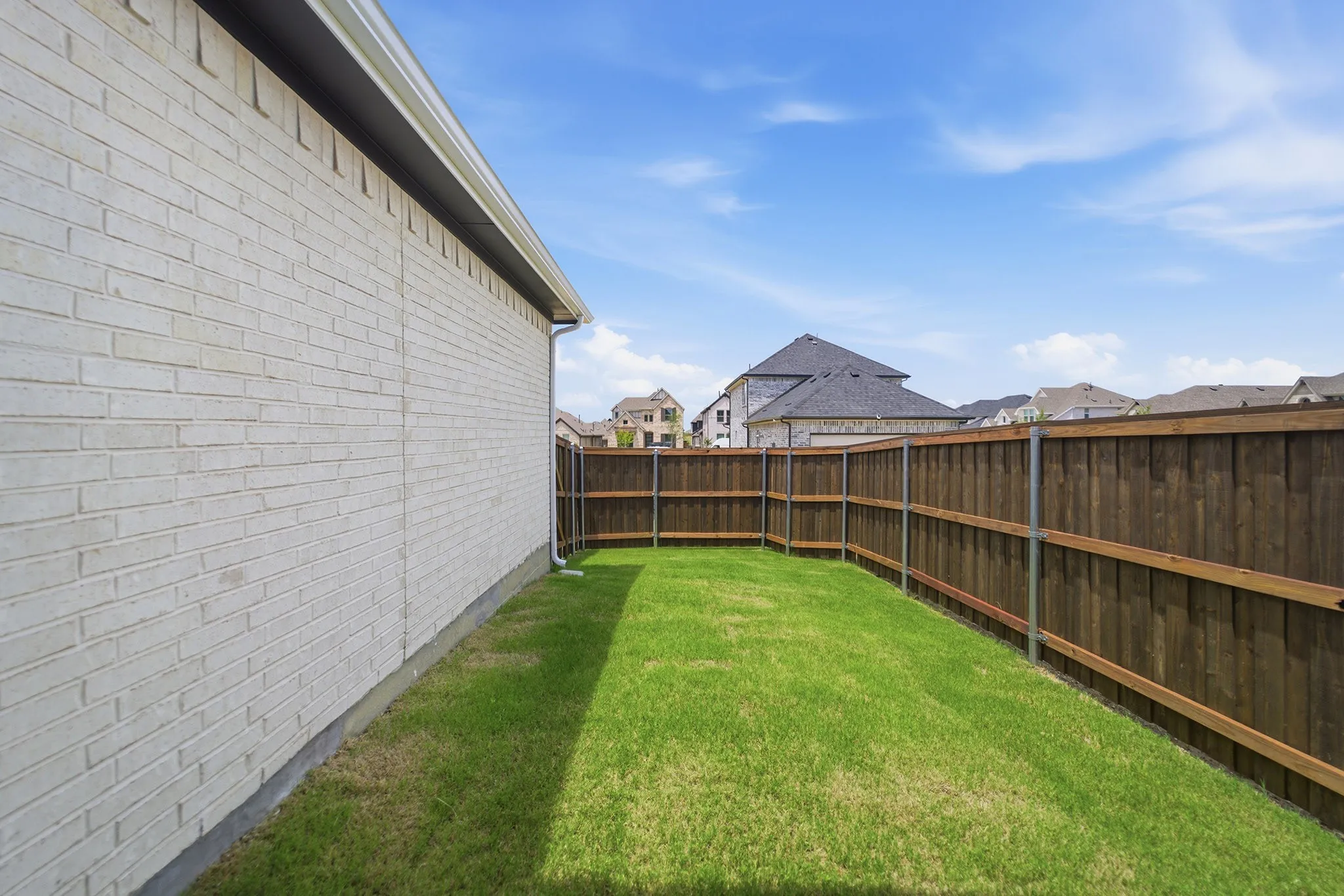 Grassed side yard featuring a light-colored brick exterior, white gutter system, and a tall wood privacy fence