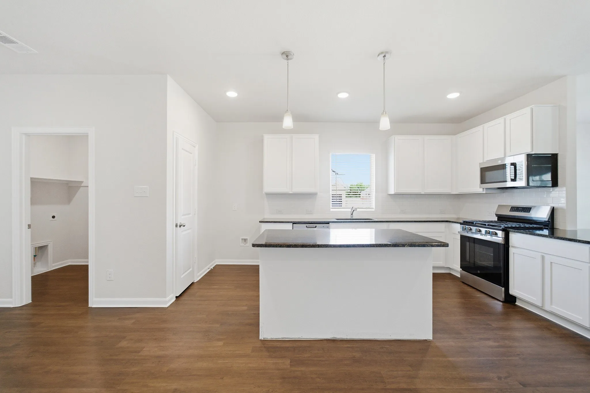 Modern kitchen featuring a central island with a dark countertop, white cabinetry, stainless steel appliances, and pendant lighting