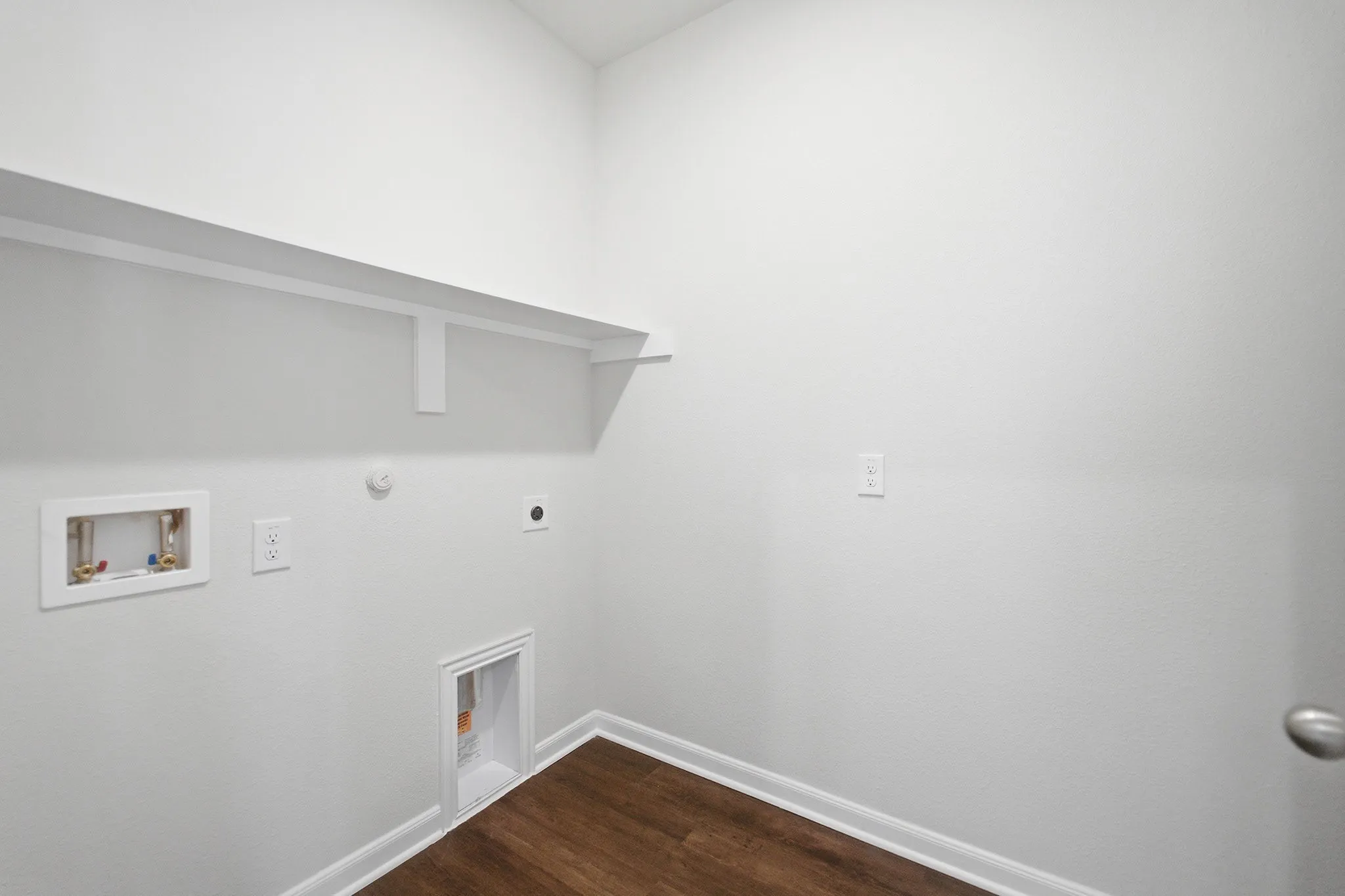 Dedicated utility space featuring a wood-finish floor, white walls, and a built-in shelf