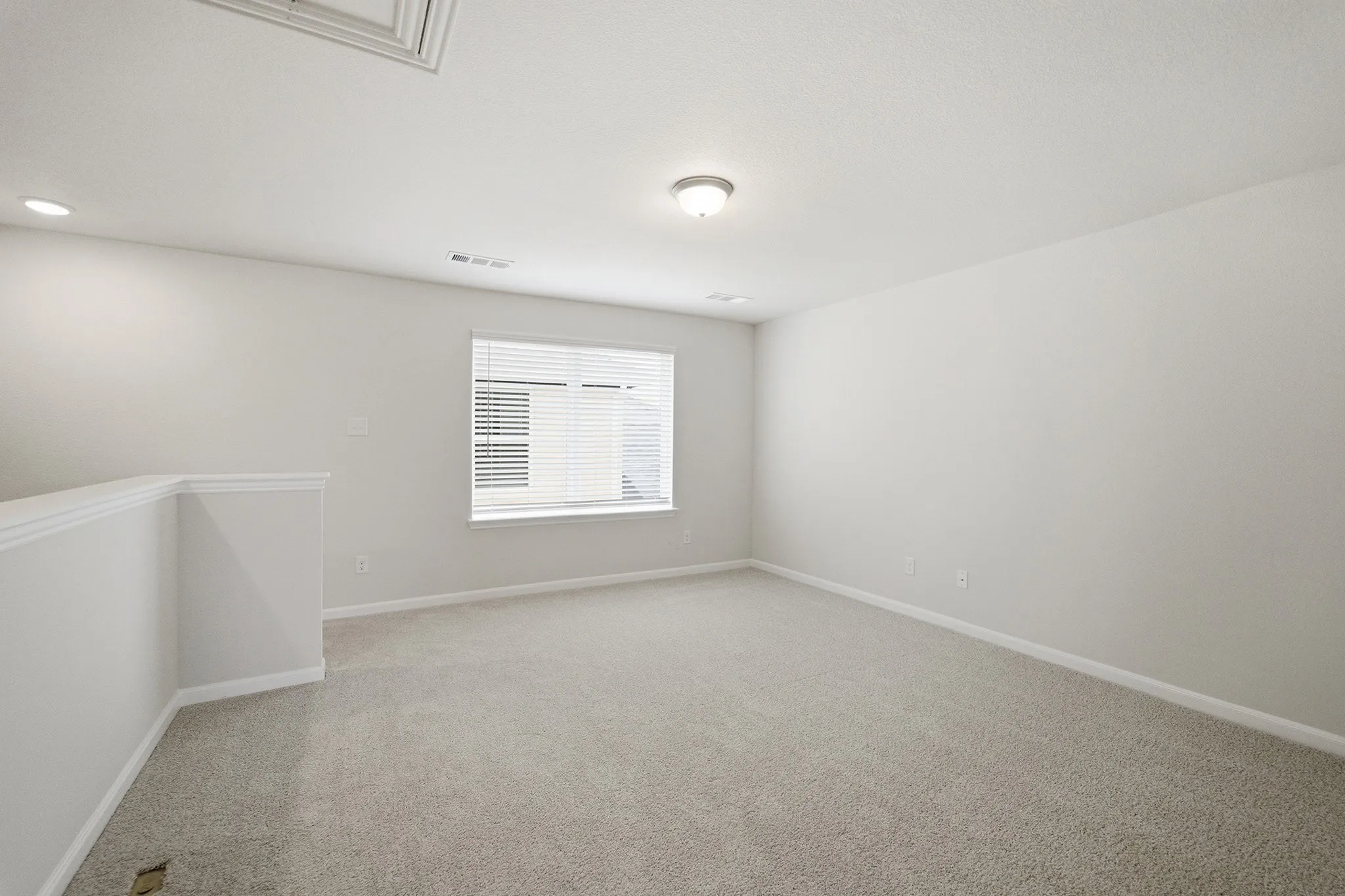 Bright room featuring light grey carpeting, recessed lighting, and a single window with blinds
