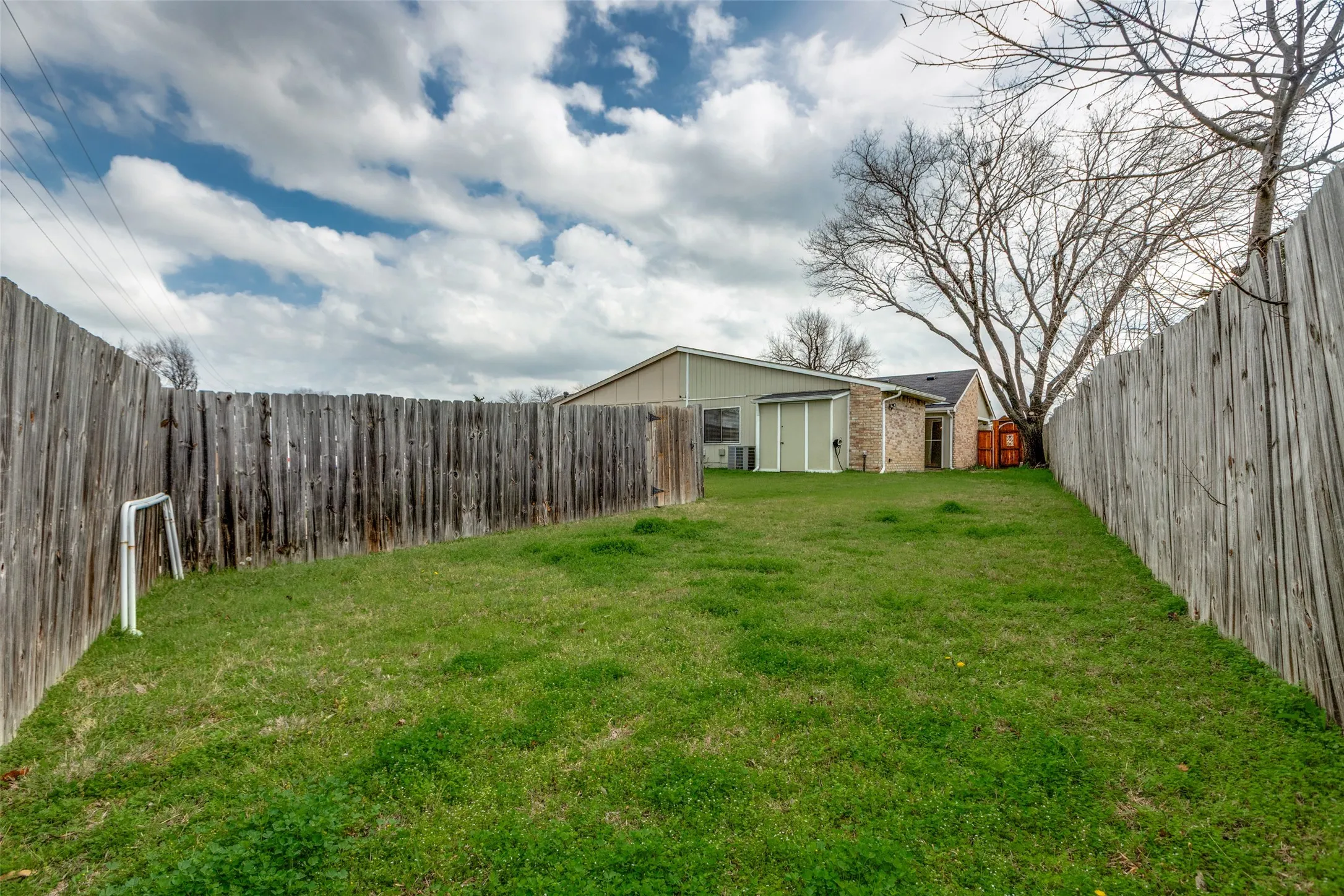 Expansive backyard featuring a lush green lawn, full wood privacy fencing, and mature trees