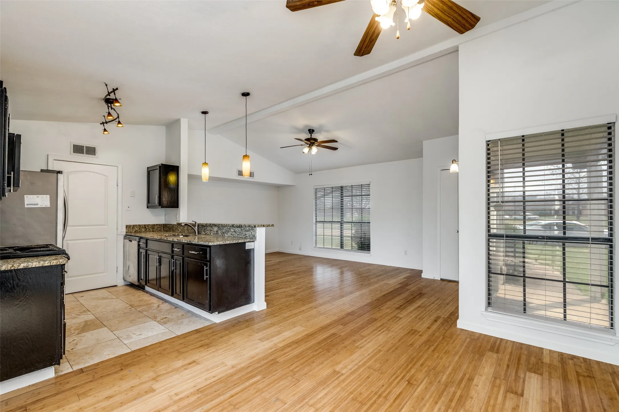 Kitchen with dark wood cabinetry, granite countertops, and tile flooring, opening to a living area with wood-finish flooring and vaulted ceilings
