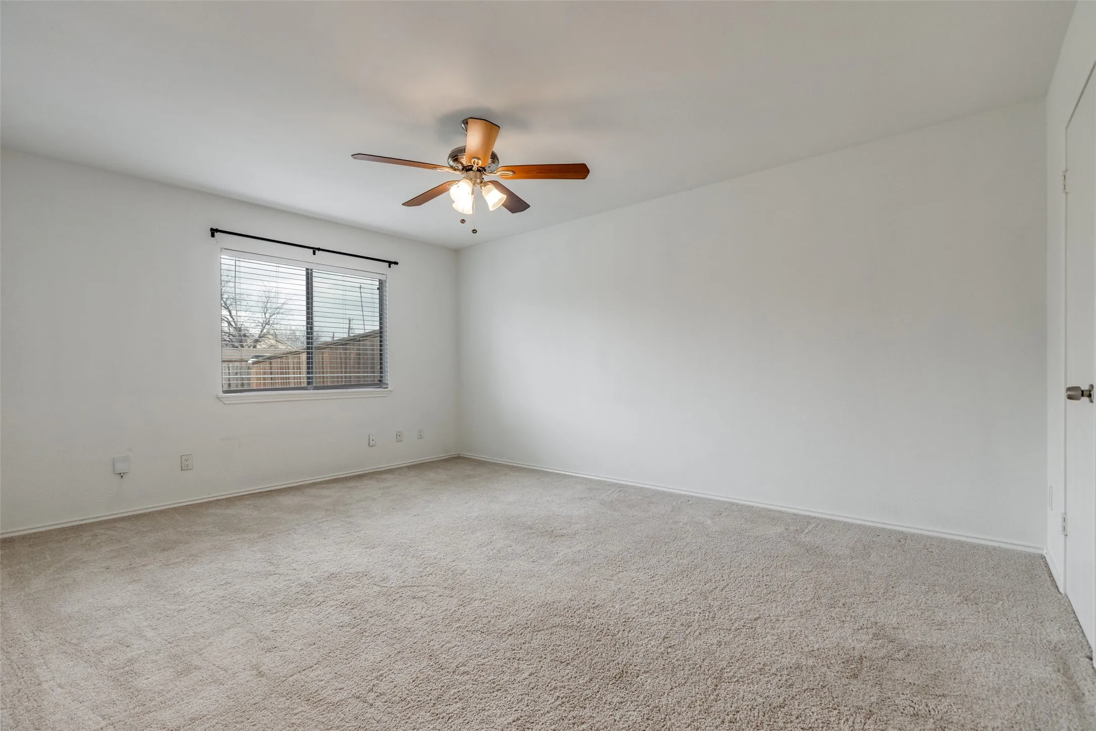 Spacious room featuring neutral carpeting, white walls, and a ceiling fan with integrated lighting