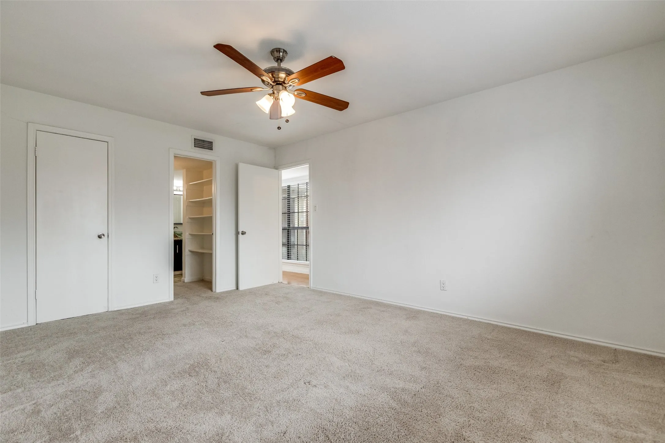 Carpeted room featuring a ceiling fan with light fixture, ample wall space, white doors, and a built-in shelving unit