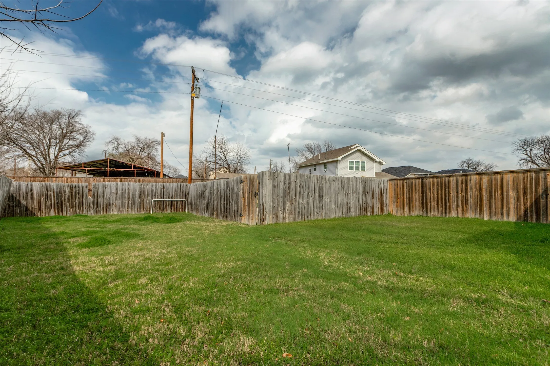Expansive fenced backyard featuring a grassy lawn, wood privacy fencing, and mature trees beyond the property line