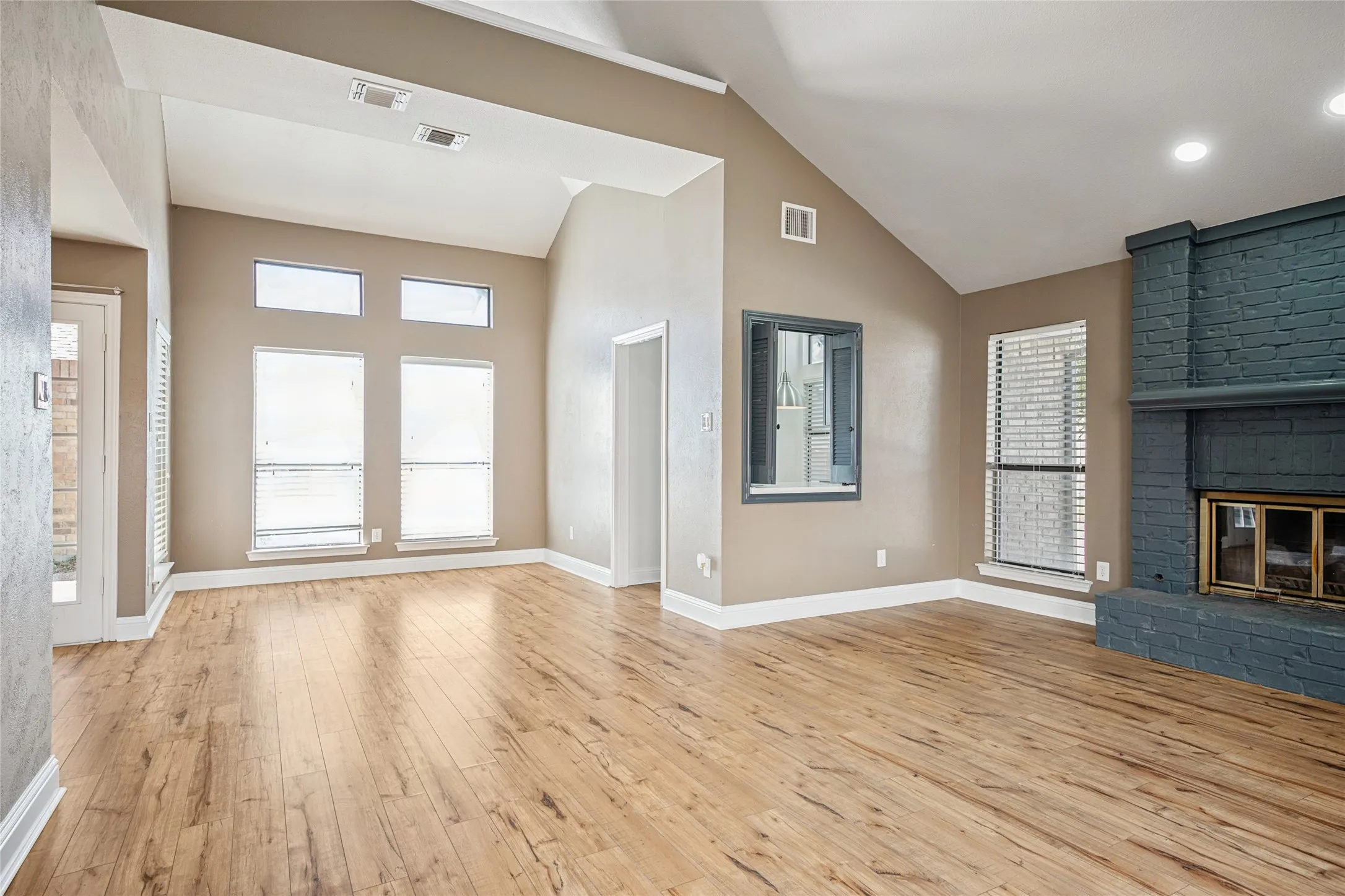 Unfurnished living room featuring a brick fireplace, visible vents, baseboards, and wood finished floors