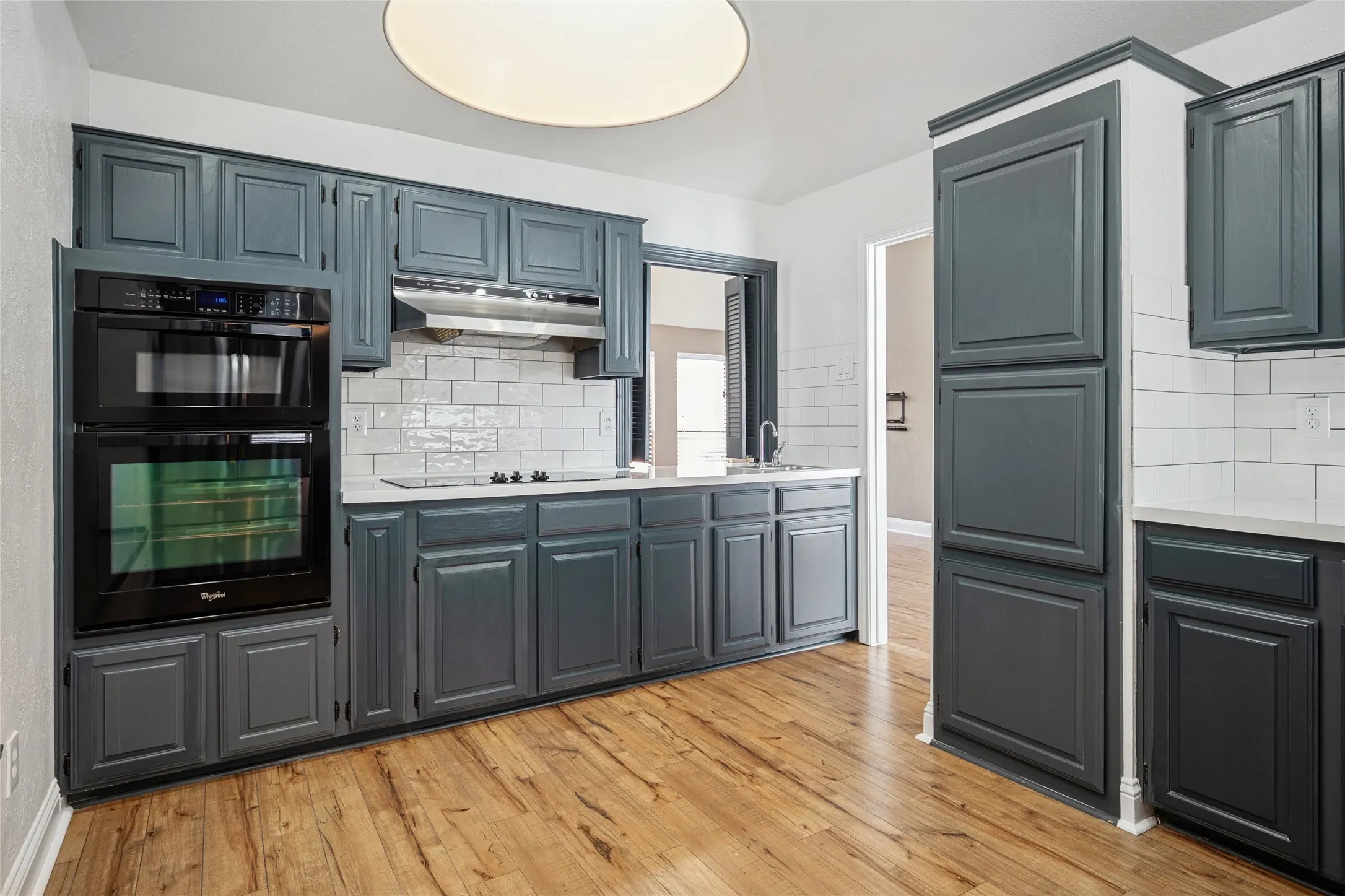 Kitchen with light countertops, light wood-style floors, a sink, under cabinet range hood, and black appliances
