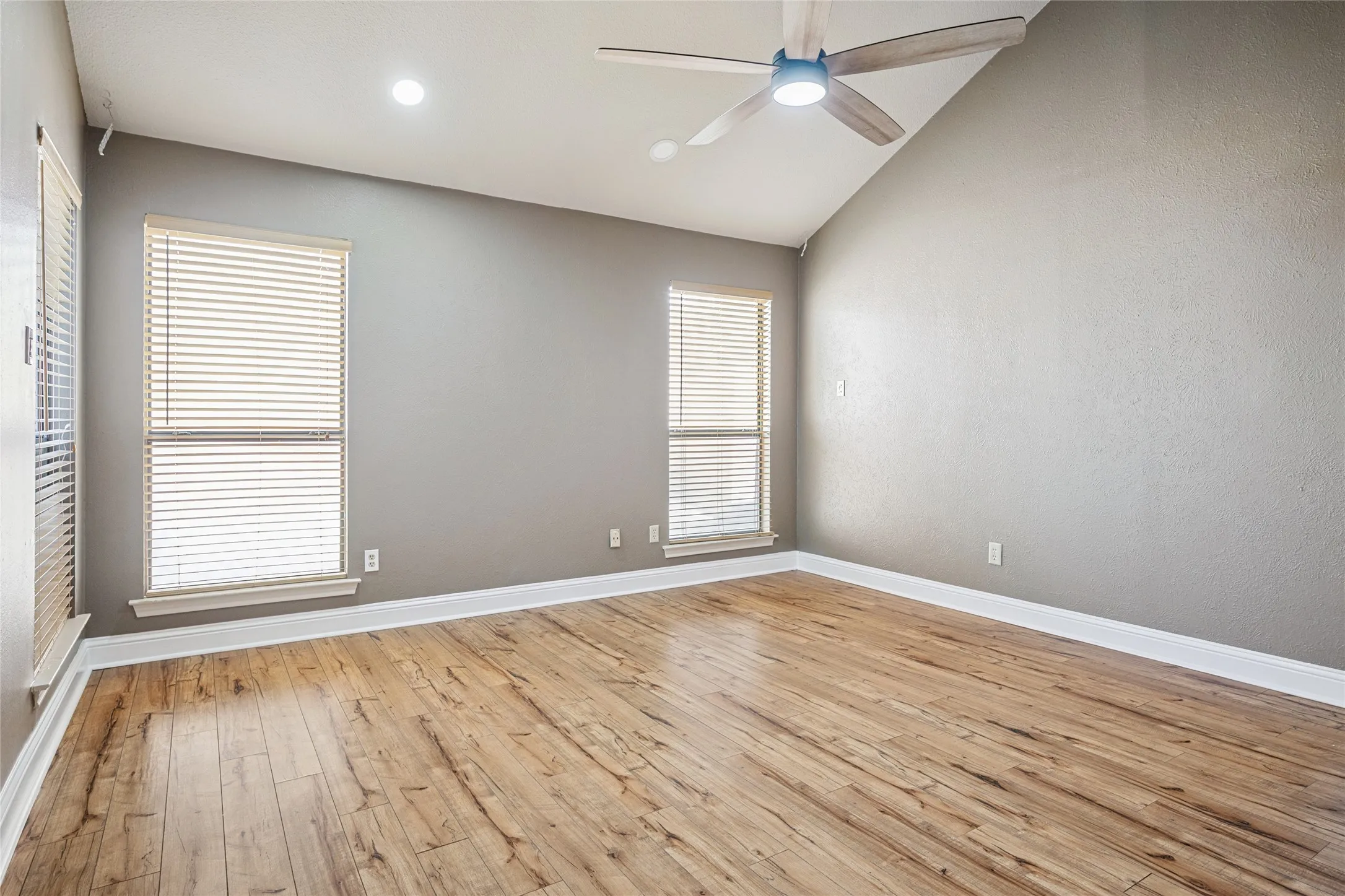 Spare room with light wood finished floors, baseboards, vaulted ceiling, and a ceiling fan