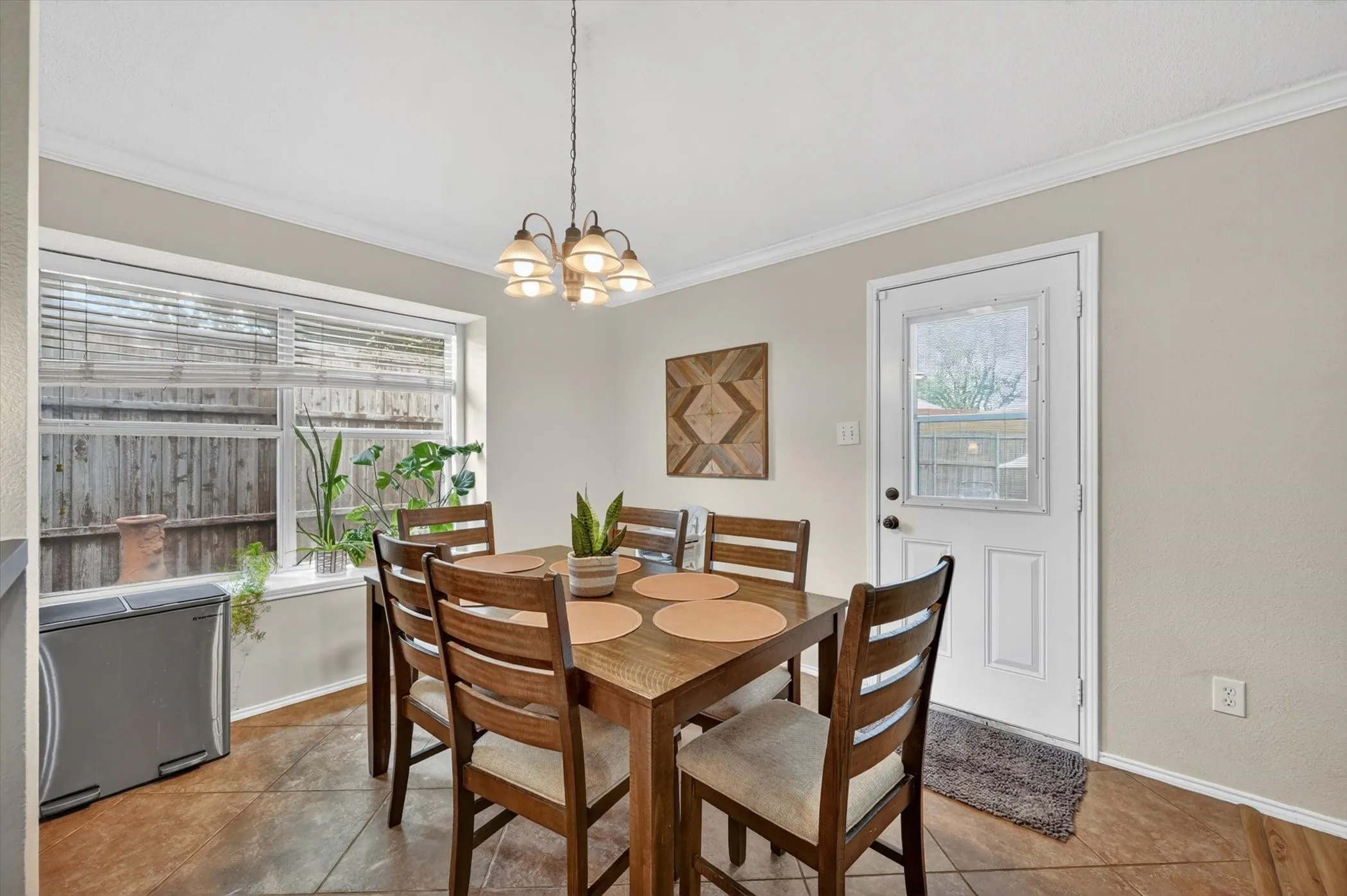 Dining space featuring a multi-pane window with blinds, a white paneled door with an upper window, a central chandelier, and tile flooring