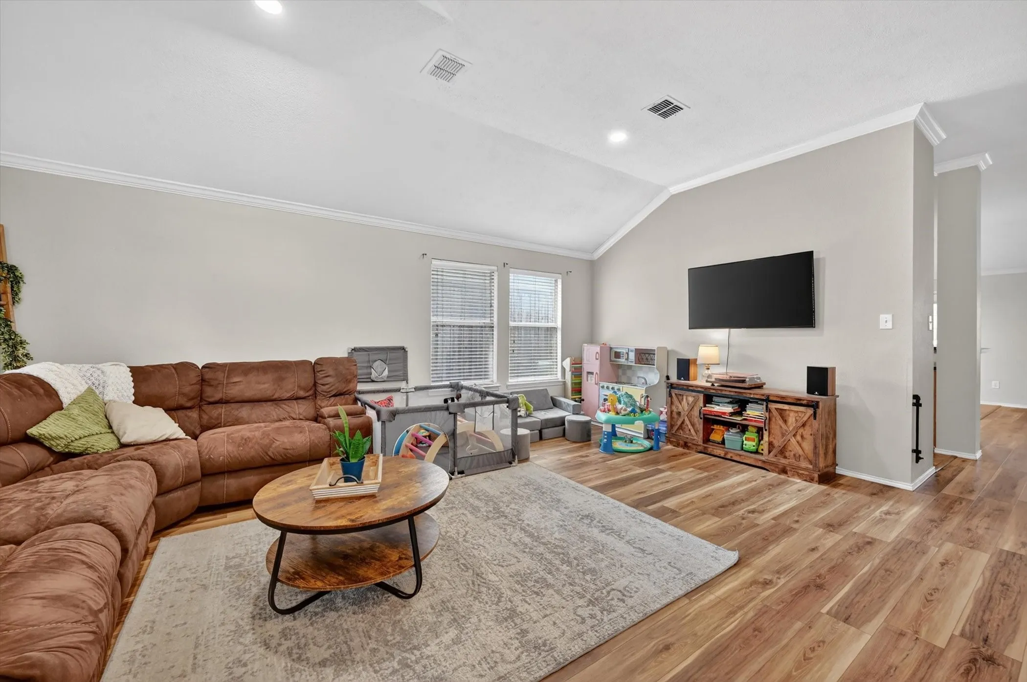 Spacious living area featuring vaulted ceilings, crown molding, wood-finish flooring, and recessed lighting