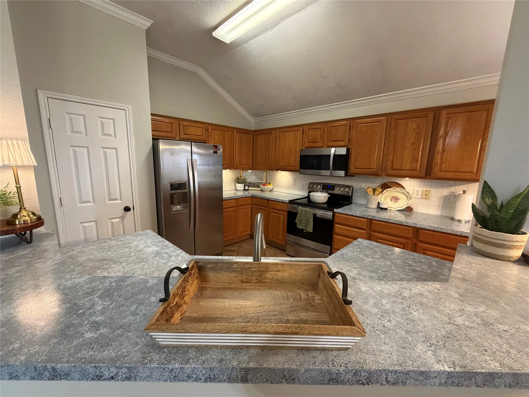 Vaulted ceiling, crown molding, wood cabinetry, white subway tile backsplash, and stainless steel appliances