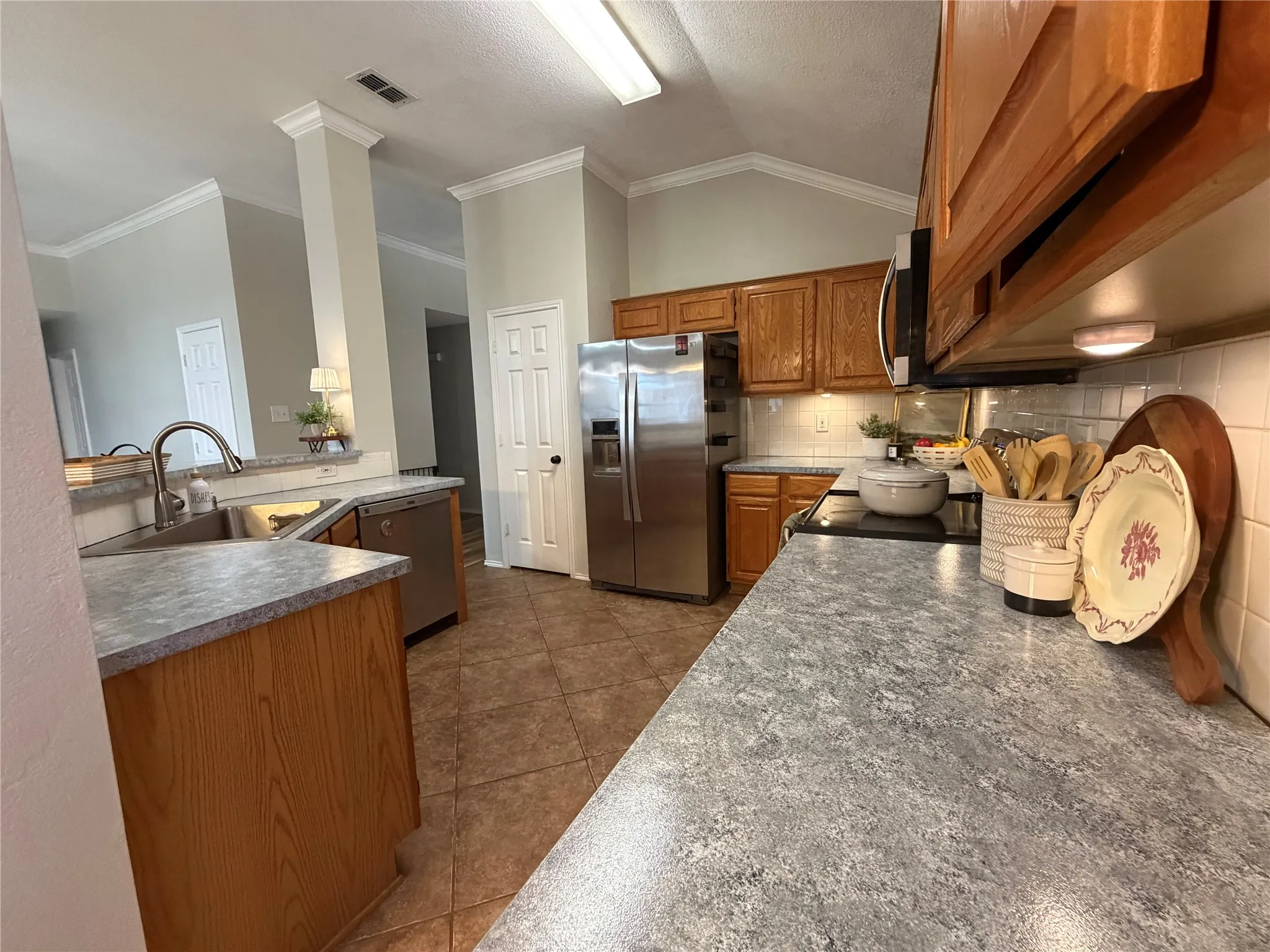 Kitchen with tile flooring, wood cabinetry, stainless steel appliances, and solid surface countertops