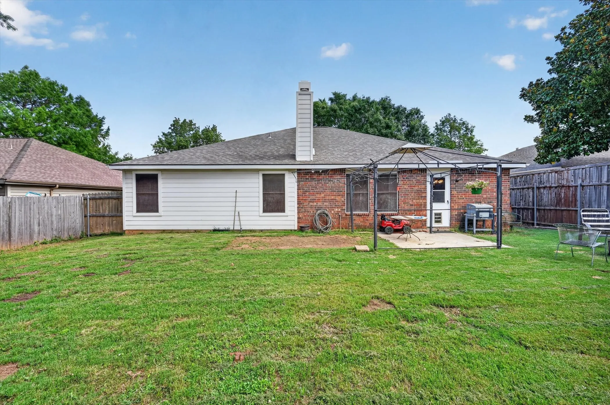 Expansive backyard featuring a brick and siding exterior, a concrete patio, and a privacy fence