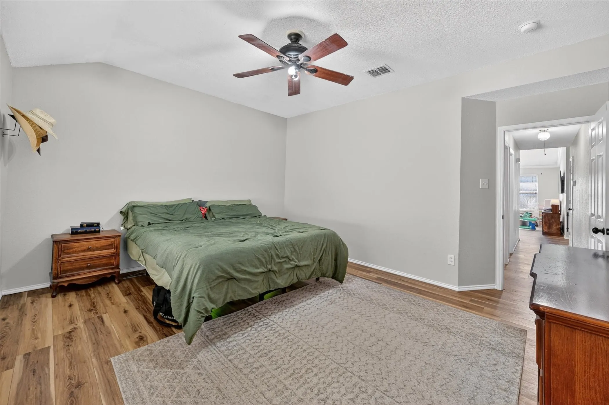 Spacious room featuring wood-finish flooring, a ceiling fan with light fixture, and light gray wall paint