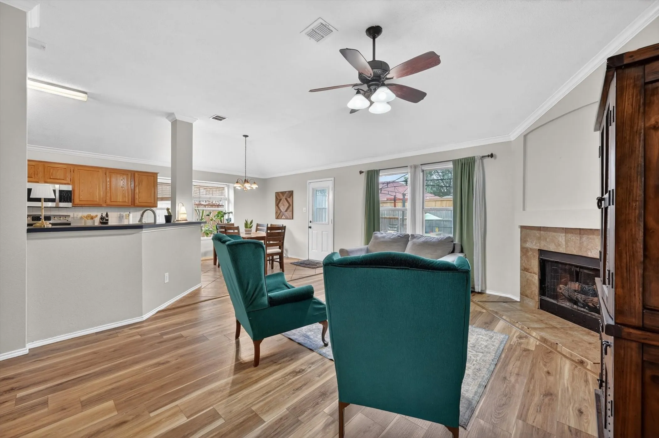 Open-concept living area featuring wood-finish flooring, a ceiling fan, and a tiled fireplace