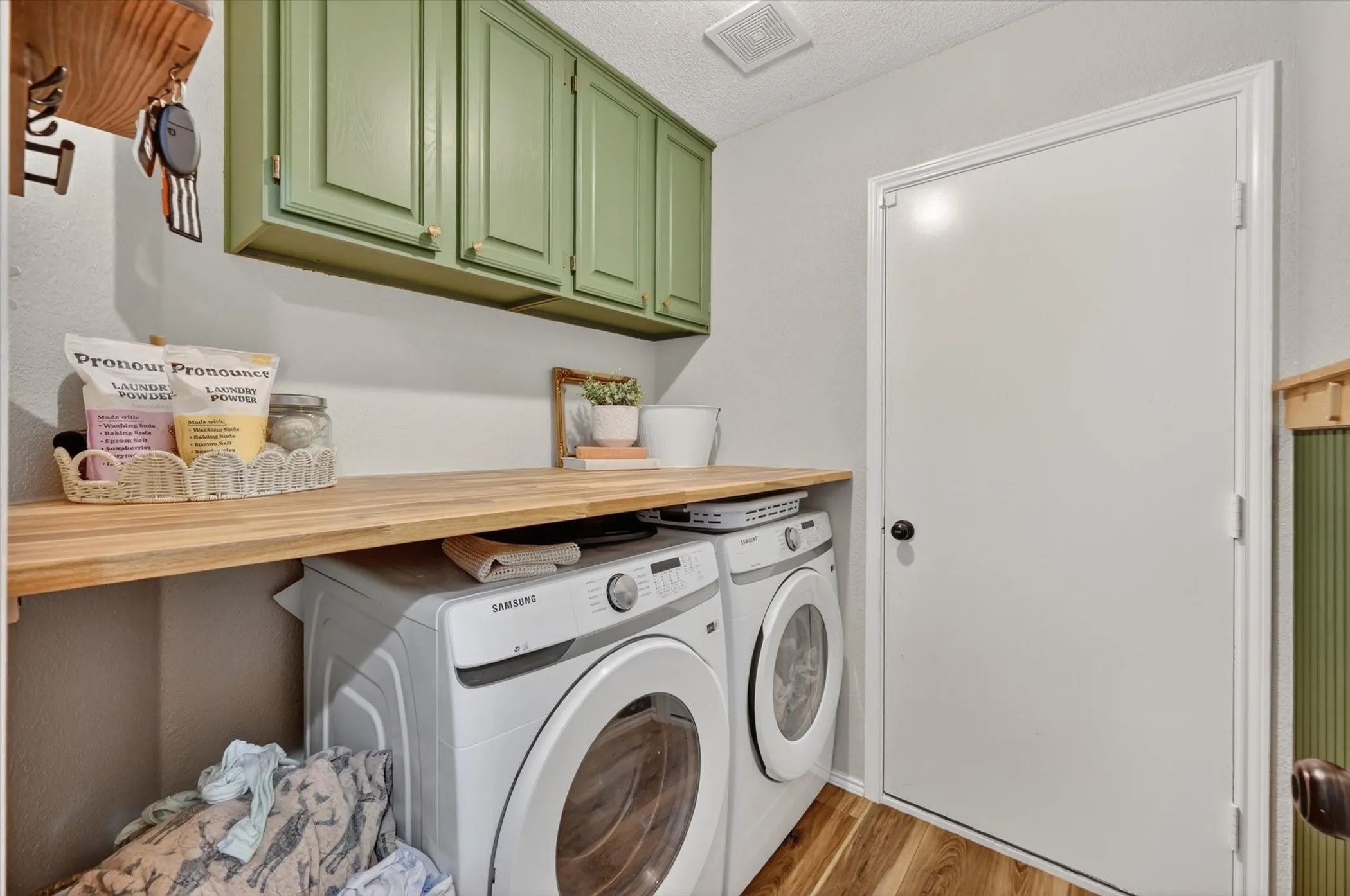 Laundry area featuring light wood-finish flooring, a white door with a black knob, and light green upper cabinetry