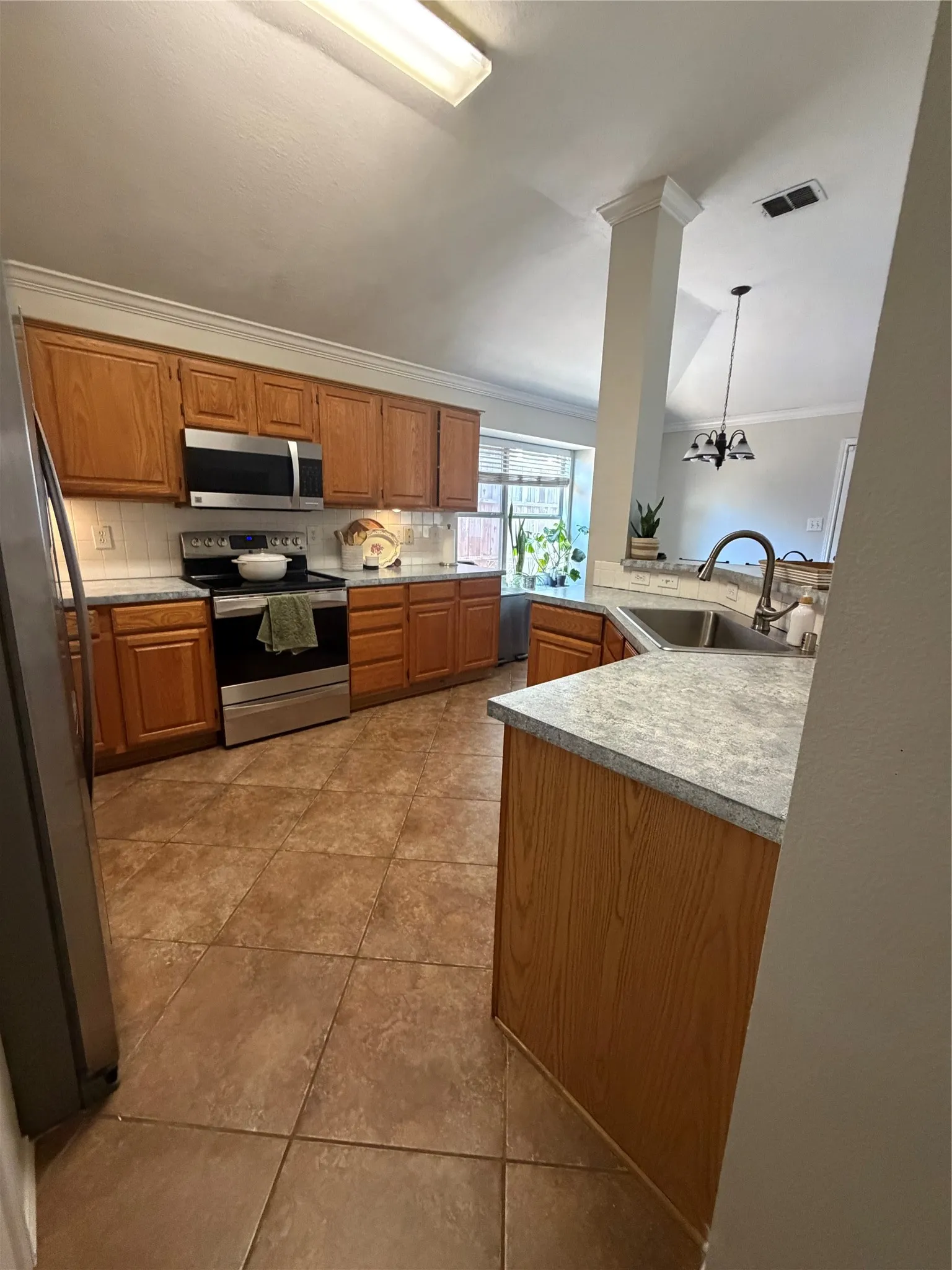 Kitchen featuring wood-finish cabinetry, stainless steel appliances, tile flooring, and a double basin sink with a high-arch faucet