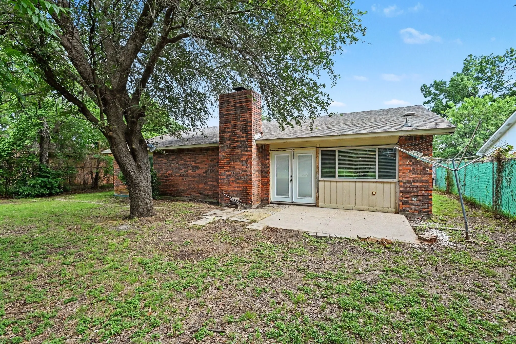 Rear exterior featuring a brick facade, integrated brick chimney, and a concrete patio