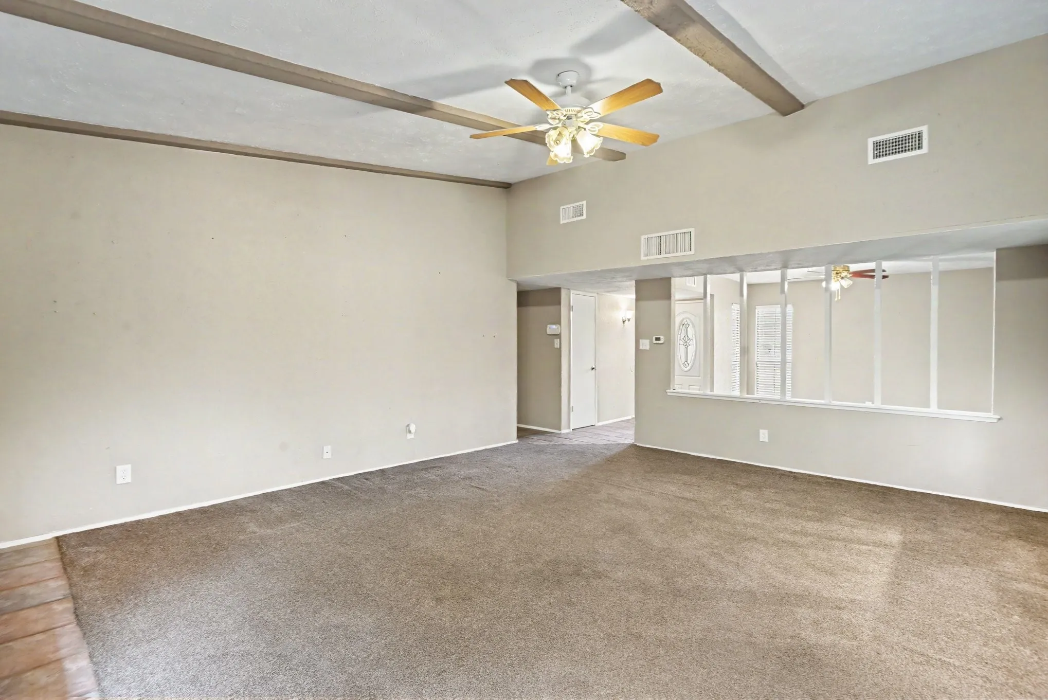 Spacious living area featuring a vaulted ceiling with exposed wood beams, a ceiling fan, and carpet flooring