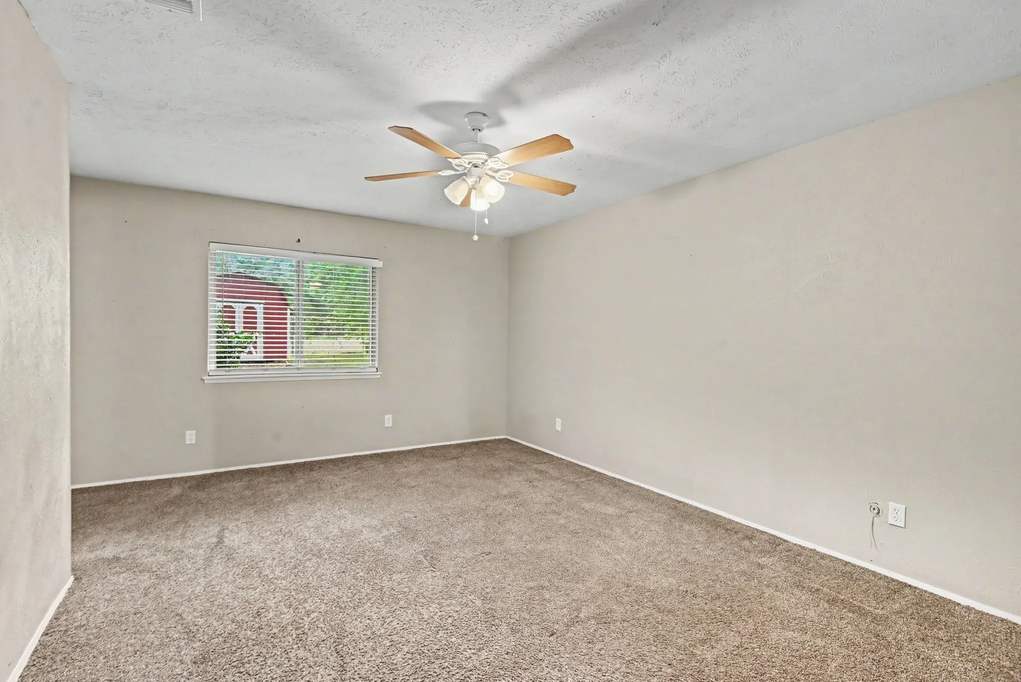 Spacious room featuring neutral carpeting, a ceiling fan with light fixture, and a window with blinds