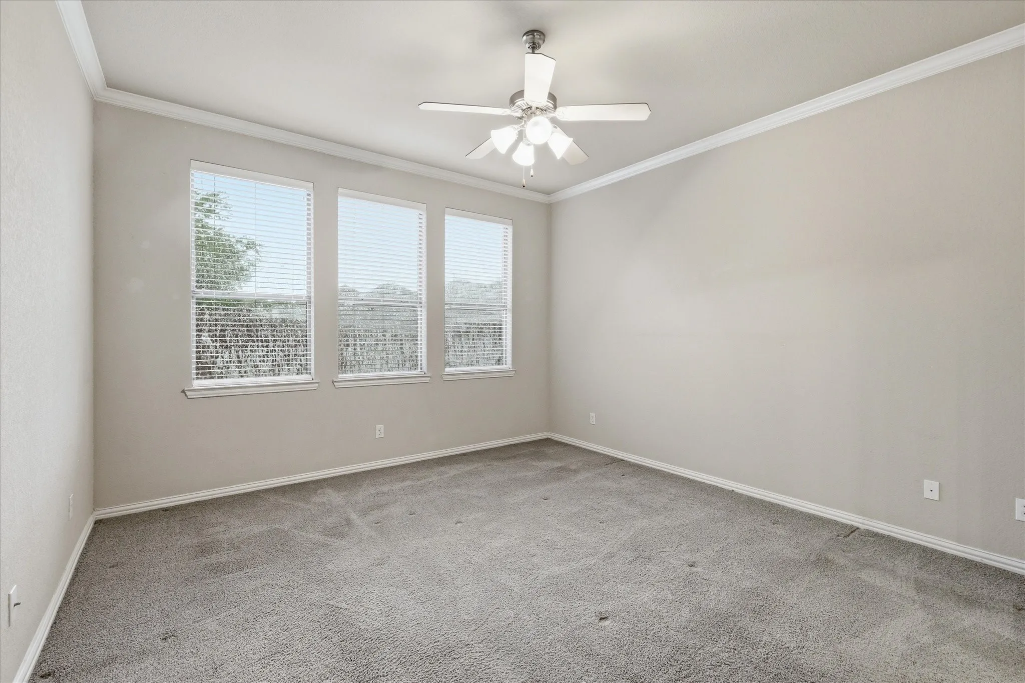 Spacious first floor primary bedroom featuring three large windows that overlook the backyard. Please note - the home has solar screens for maximum energy efficiency. It was raining on the day of the photoshoot; therefore, you will notice the rain on the screens in the photos.