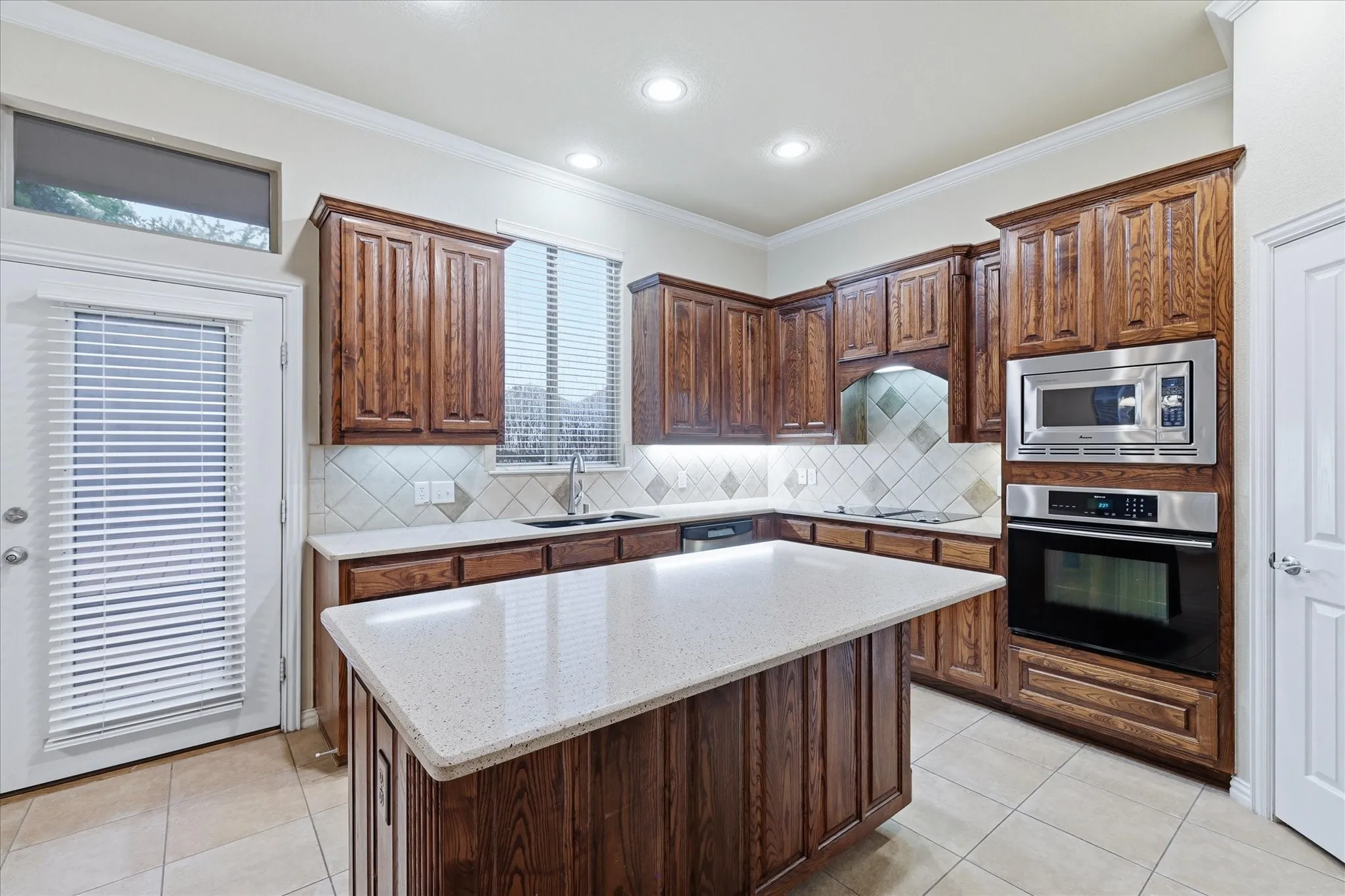 Kitchen featuring rich wood cabinetry, light-toned Corian countertops, tile flooring, stainless steel built-in appliances (mostly Jenn-Air brand), and large walk-in pantry.