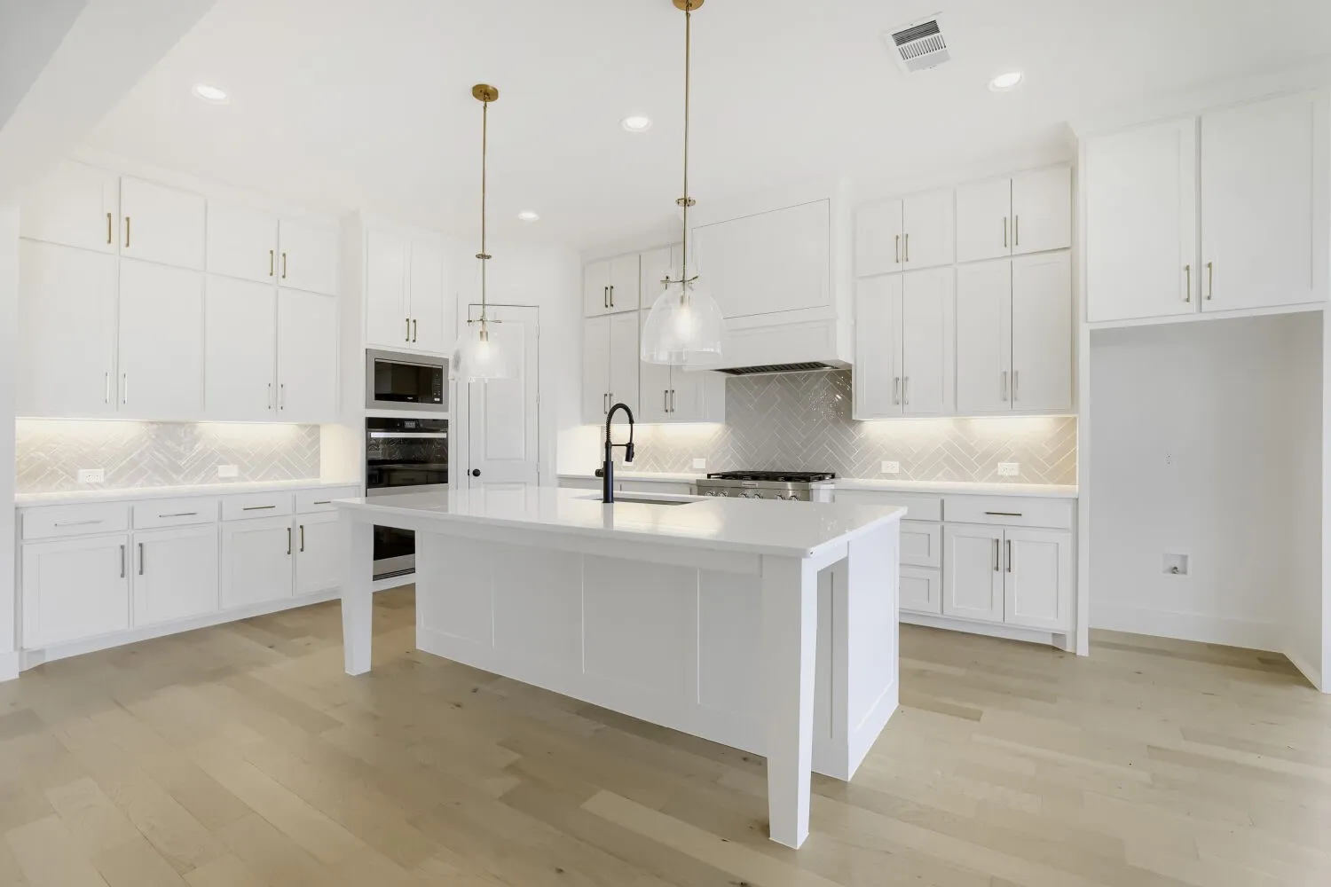 Spacious kitchen featuring an expansive center island, white cabinetry, integrated stainless steel appliances, herringbone tile backsplash, and light wood-finish flooring