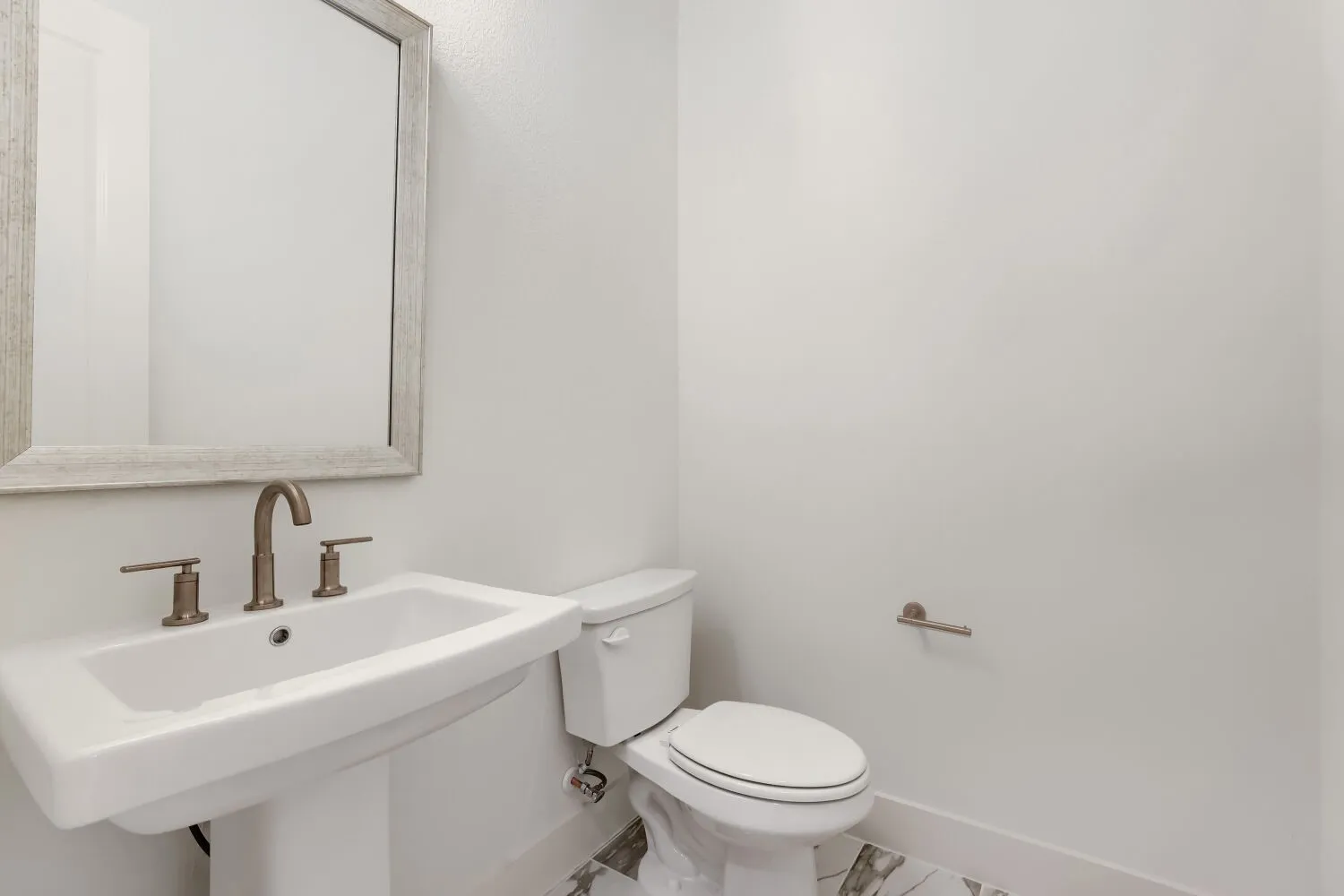 Pedestal sink with bronze-finish faucet, mirror with textured frame, and tiled flooring