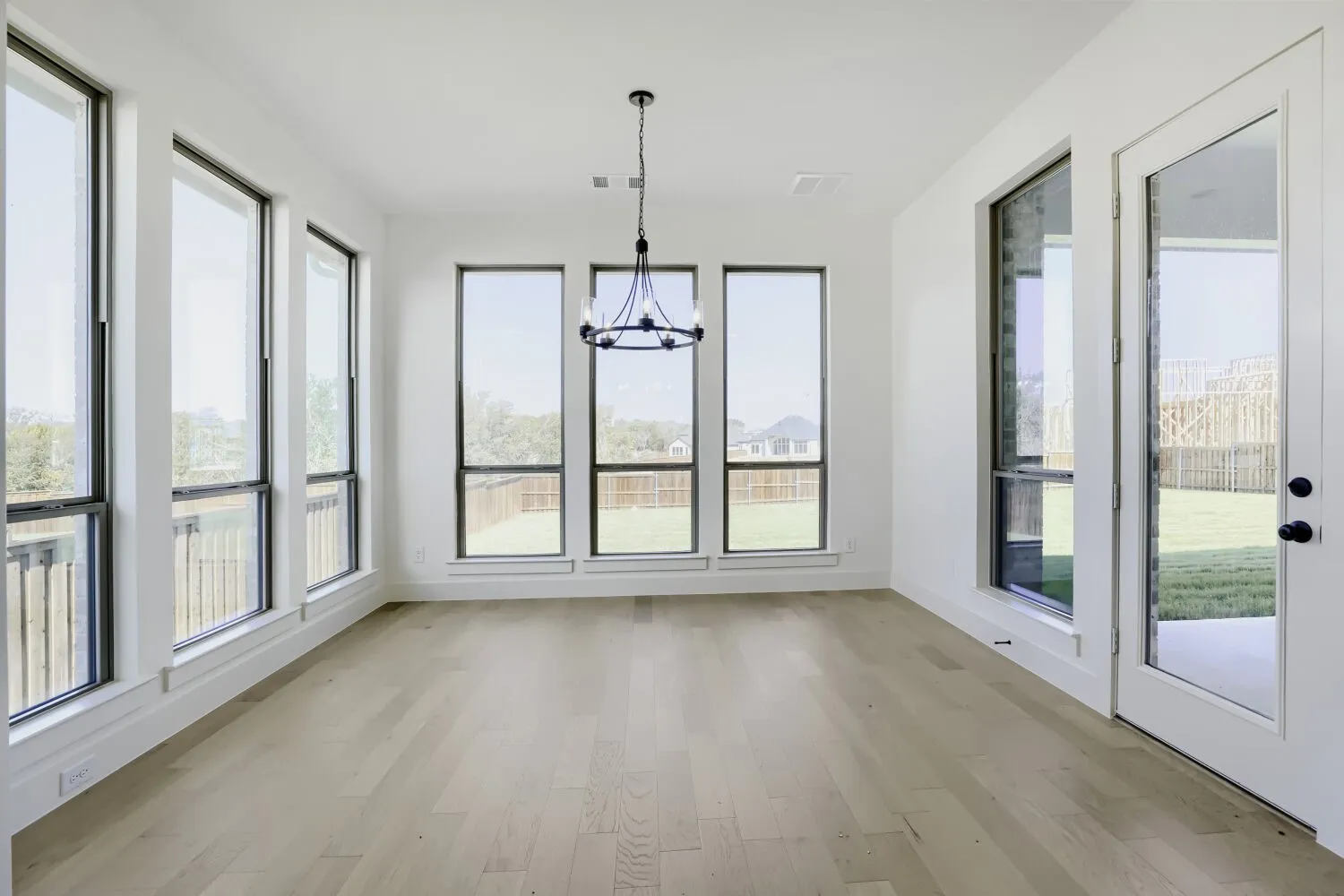 Light wood-finish flooring, multiple expansive windows, contemporary chandelier, white walls, and a glass-paneled exterior door