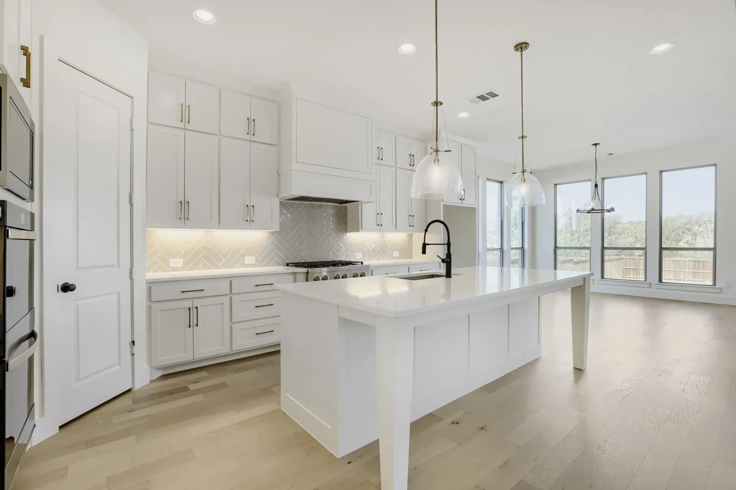 Kitchen featuring an oversized island, pendant lighting, built-in stainless steel appliances, a herringbone tile backsplash, and light wood-finish flooring