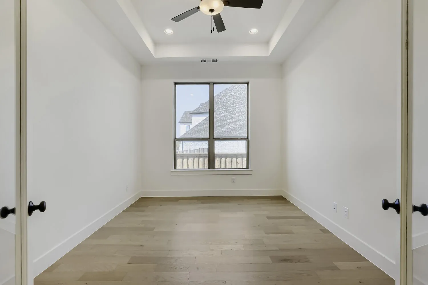 Tray ceiling with recessed lighting and a ceiling fan, wood-finish flooring, and a large window